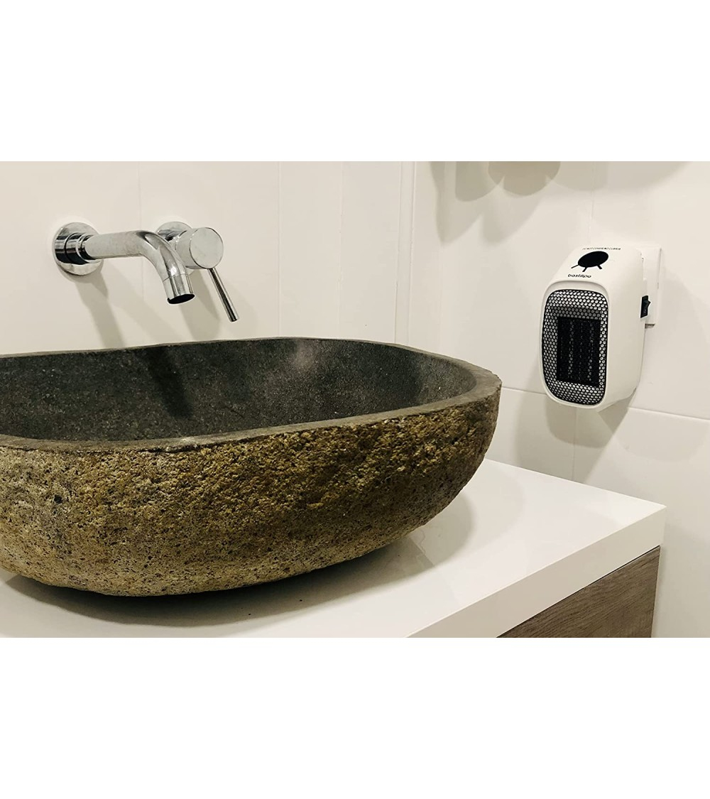 Piccolo termoventilatore elettrico bianco montato su una parete piastrellata bianca accanto a un lavabo in pietra.