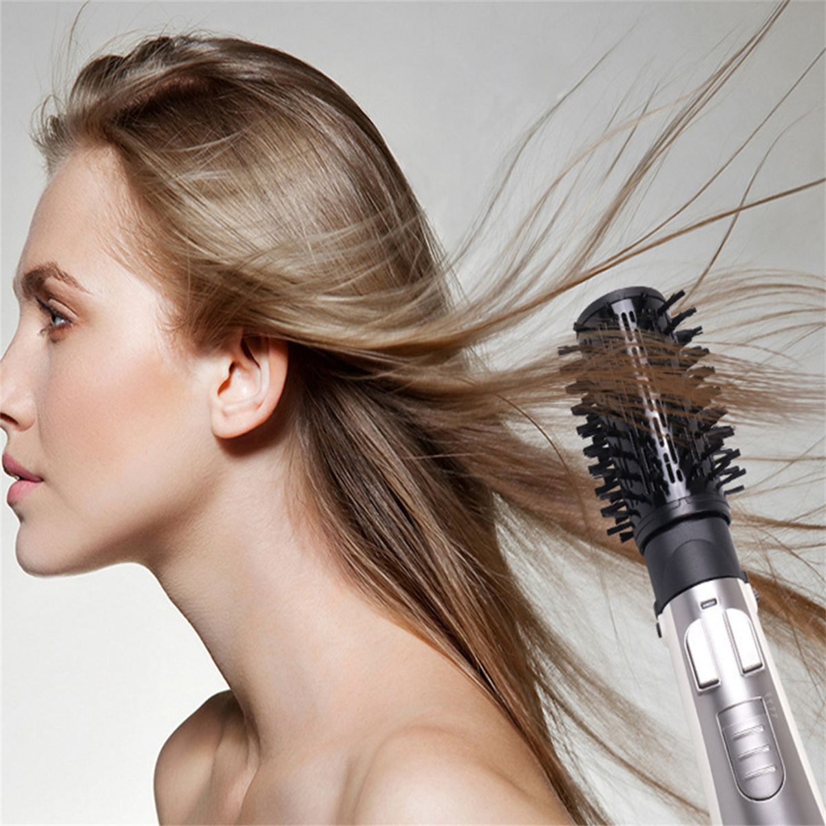 Blonde Frau, deren Haare mit einer rotierenden Haarbürste gestylt werden. Grauer Hintergrund.