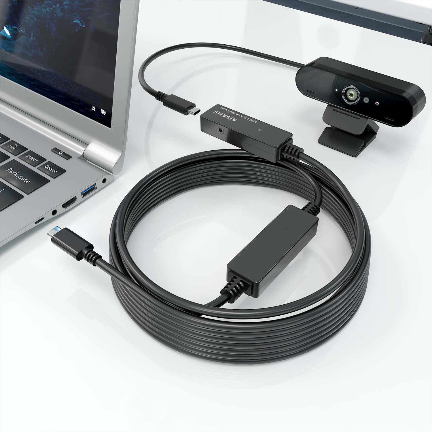 Laptop, webcam e configurazione cavo. Cavo nero li collega. Superficie bianca. Webcam in alto.