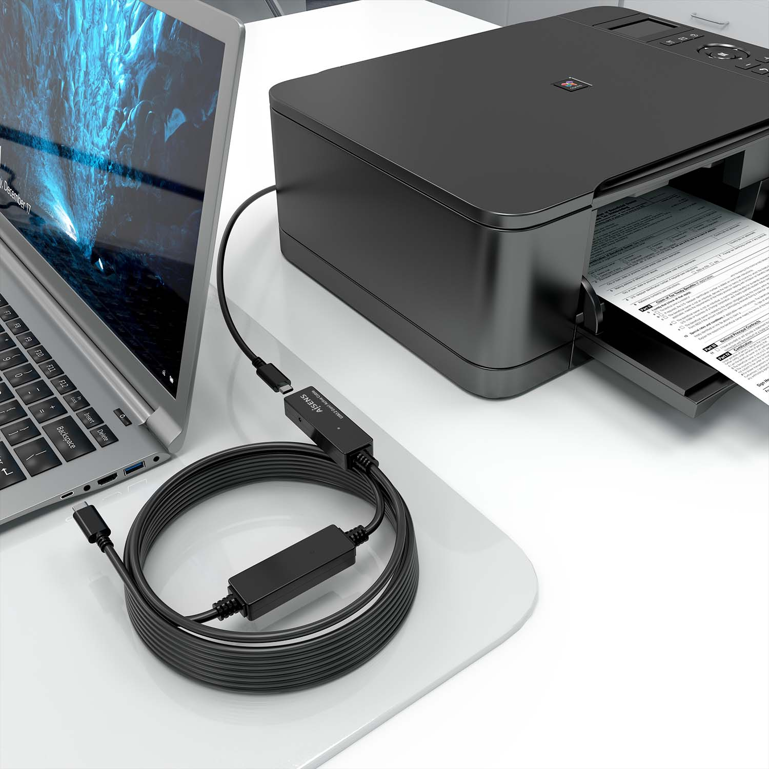 Laptop e stampante con un cavo nero che li collega su una superficie bianca.