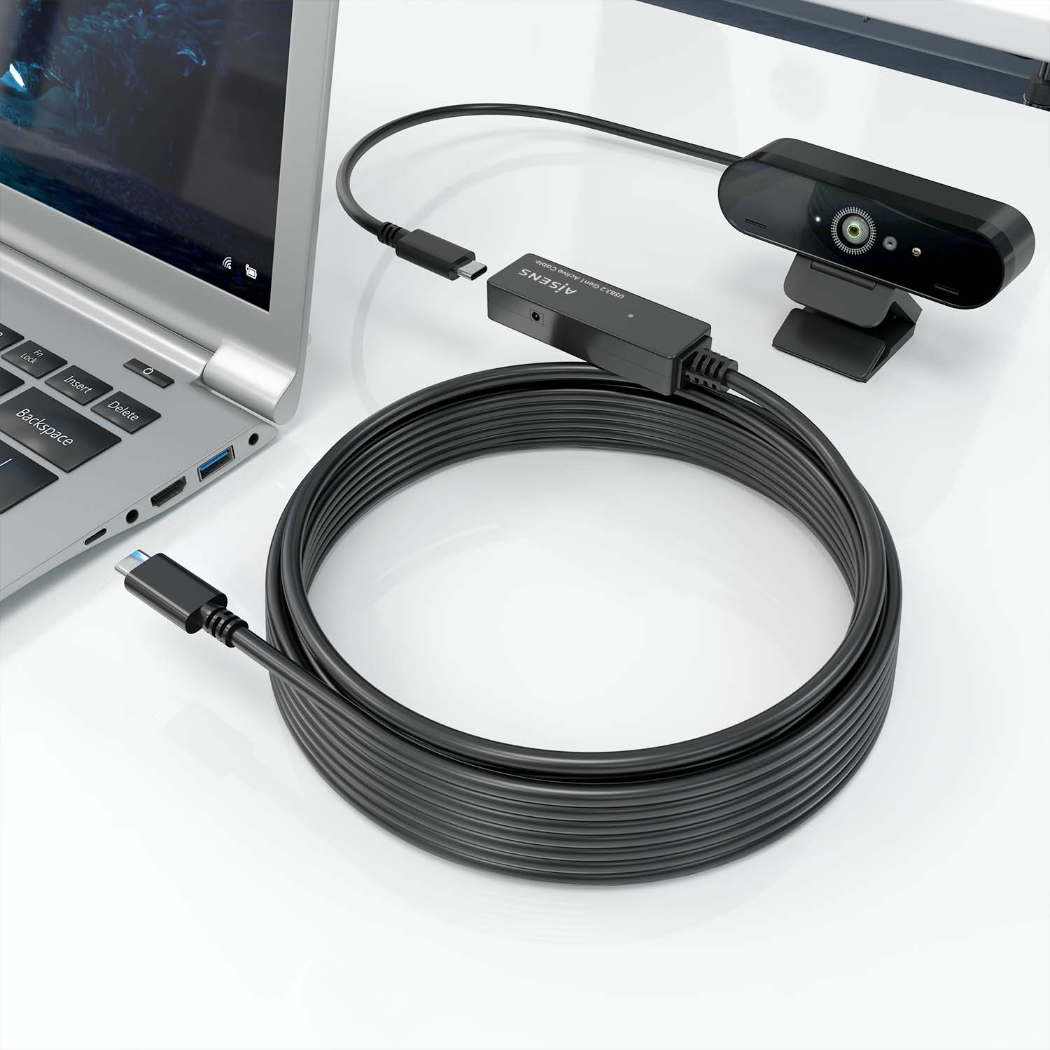 Una webcam nera e un cavo nero arrotolato collegato a un laptop su una superficie bianca.