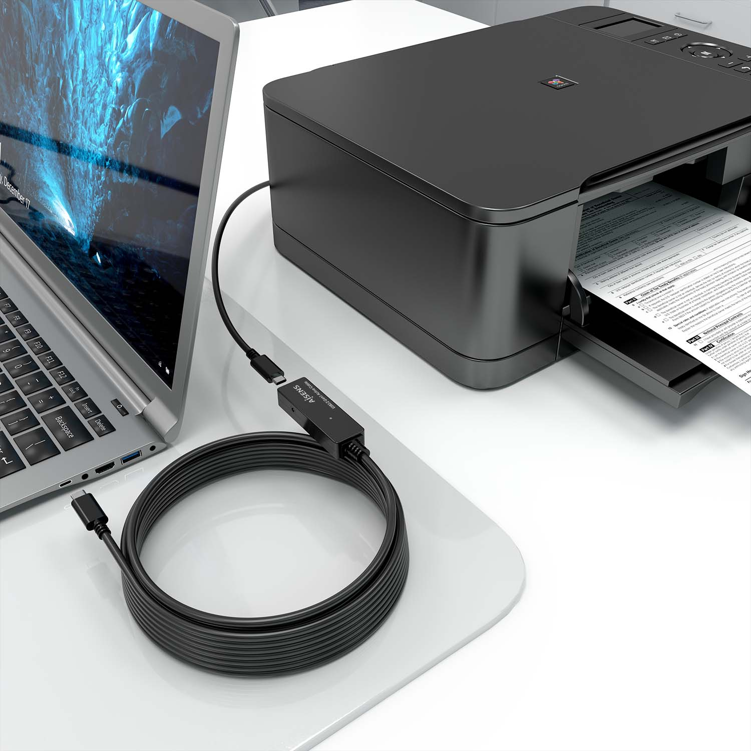 Laptop, stampante e un cavo USB nero che li collega, su una superficie bianca.