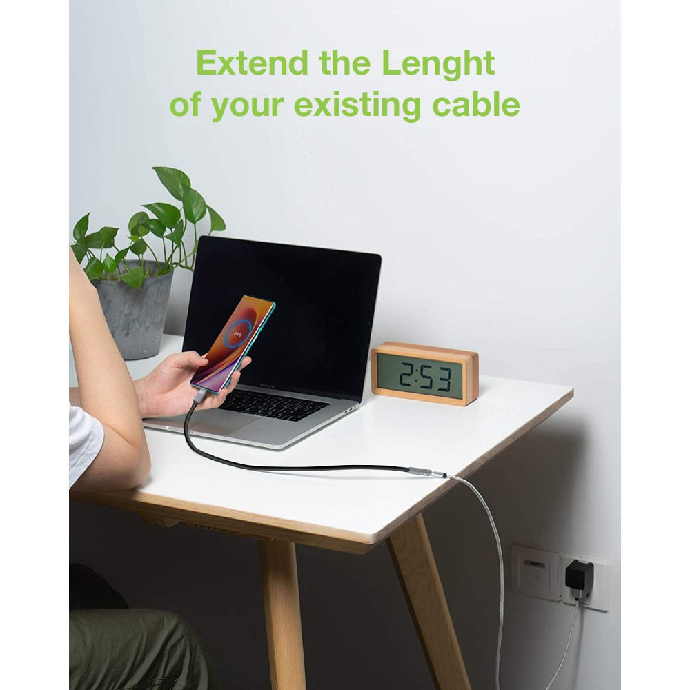 Personne utilisant un téléphone connecté à un ordinateur portable via un câble noir. Bureau avec horloge et plante.