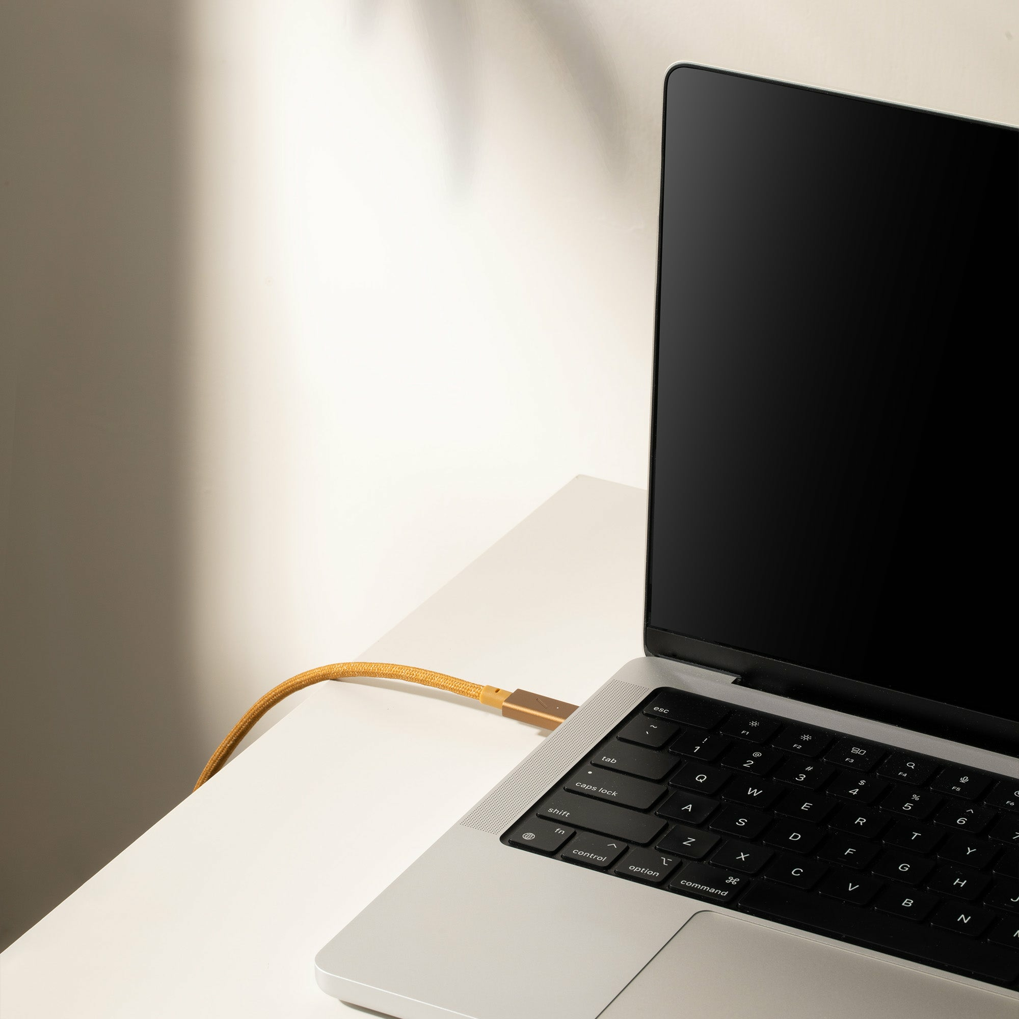 Laptop con cavo USB-C dorato collegato. Scrivania bianca e ombra.