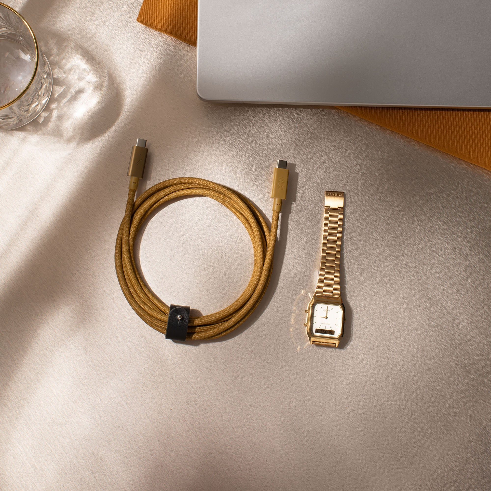 Cavo USB-C dorato, orologio e laptop su superficie satinata. Vista dall'alto.