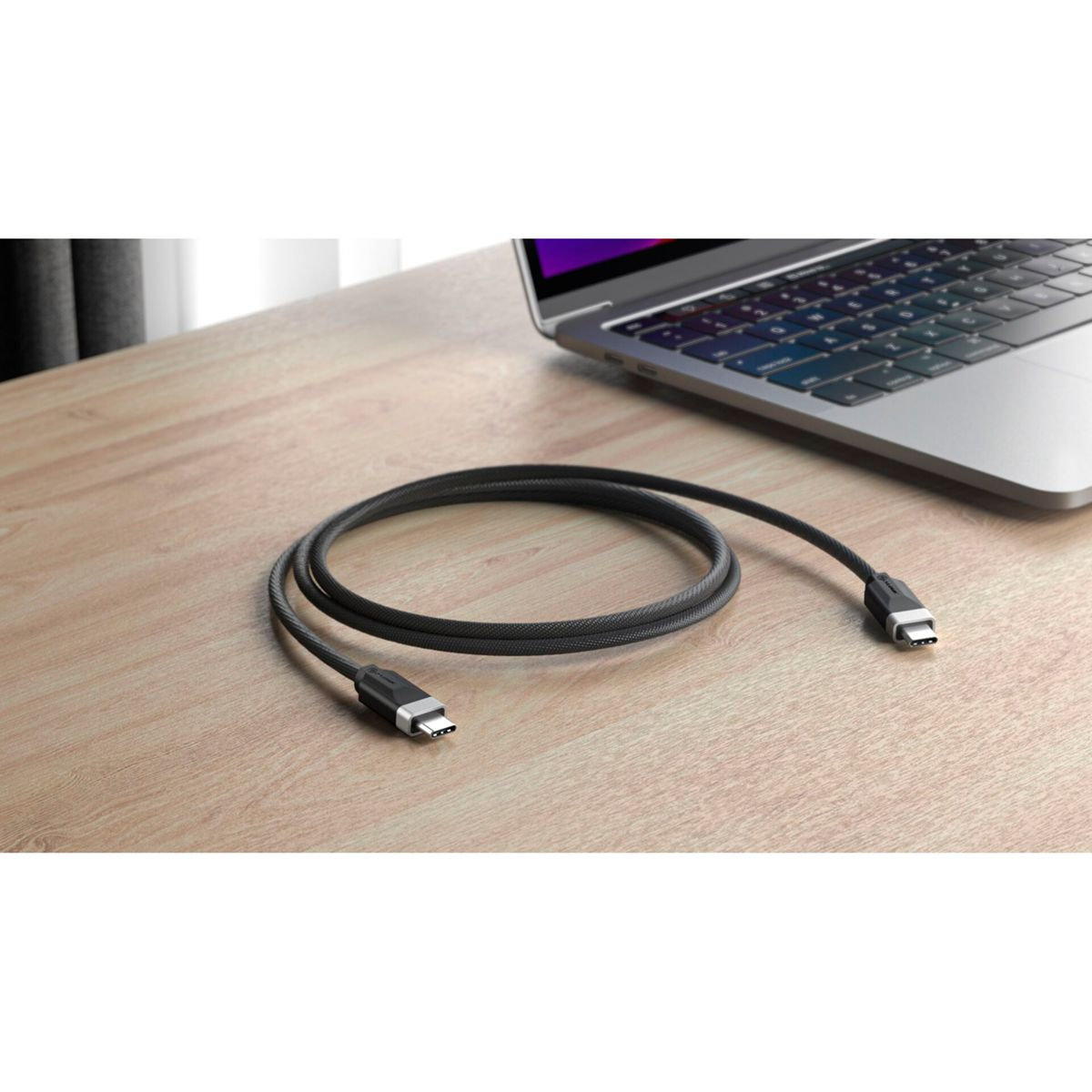 Cavo USB-C nero su scrivania in legno vicino a un laptop aperto.