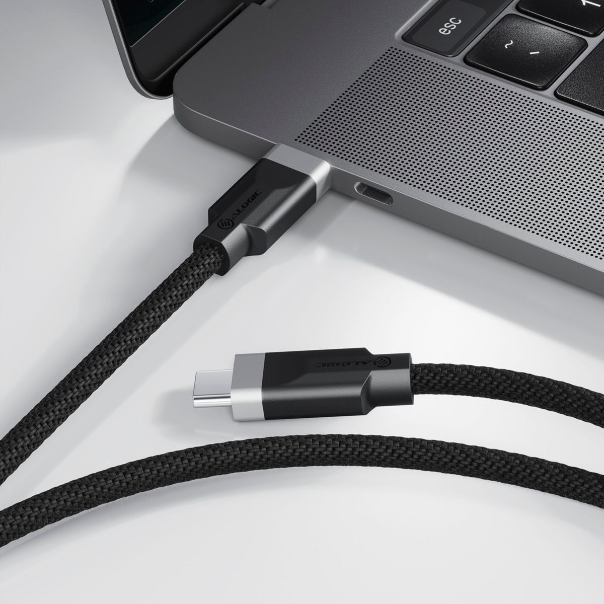 Un cavo USB-C nero collegato a un laptop. Il cavo è intrecciato e su una superficie bianca.