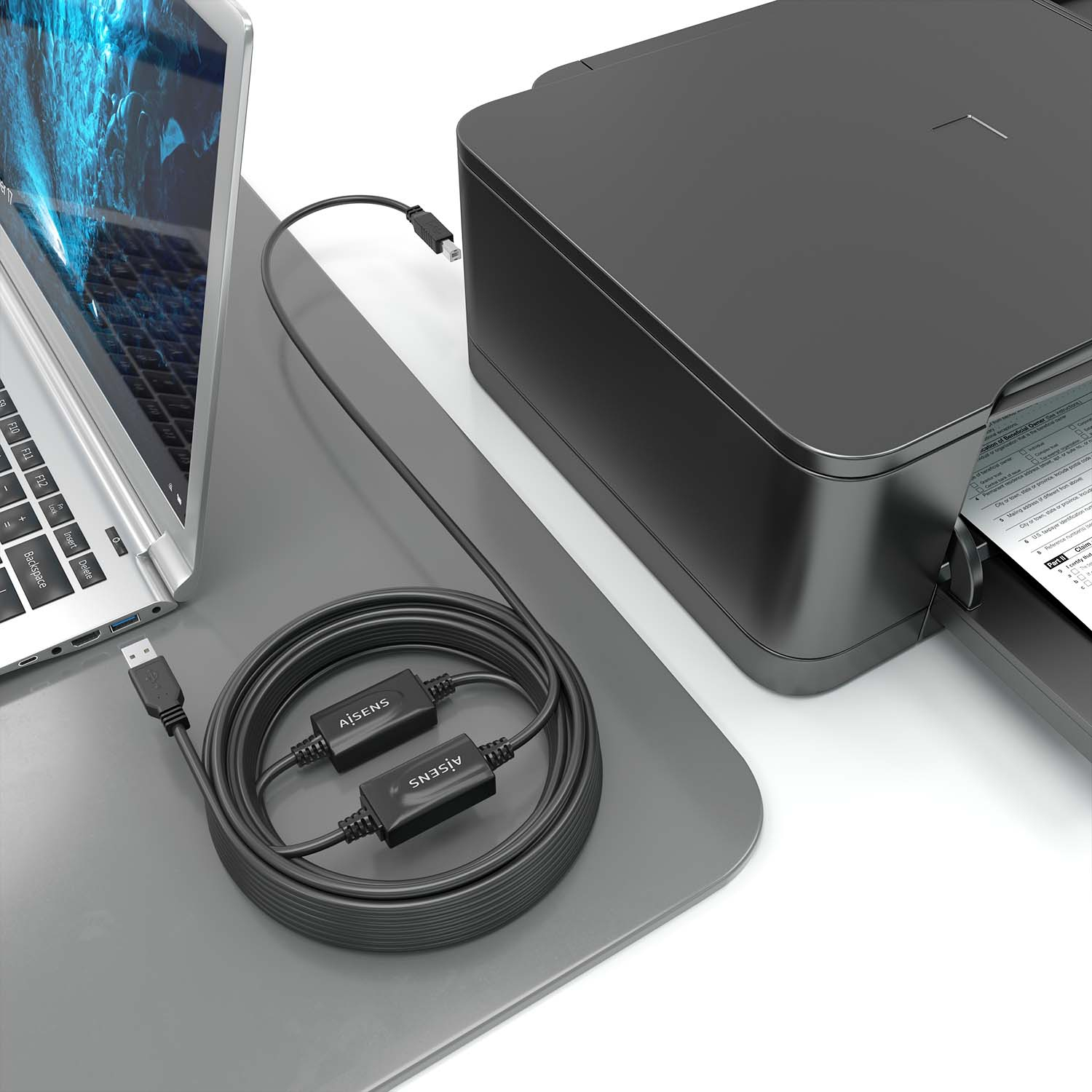 Een laptop, een printer en een zwarte USB-kabel die ze verbindt op een grijs oppervlak. De printer is aan het printen.