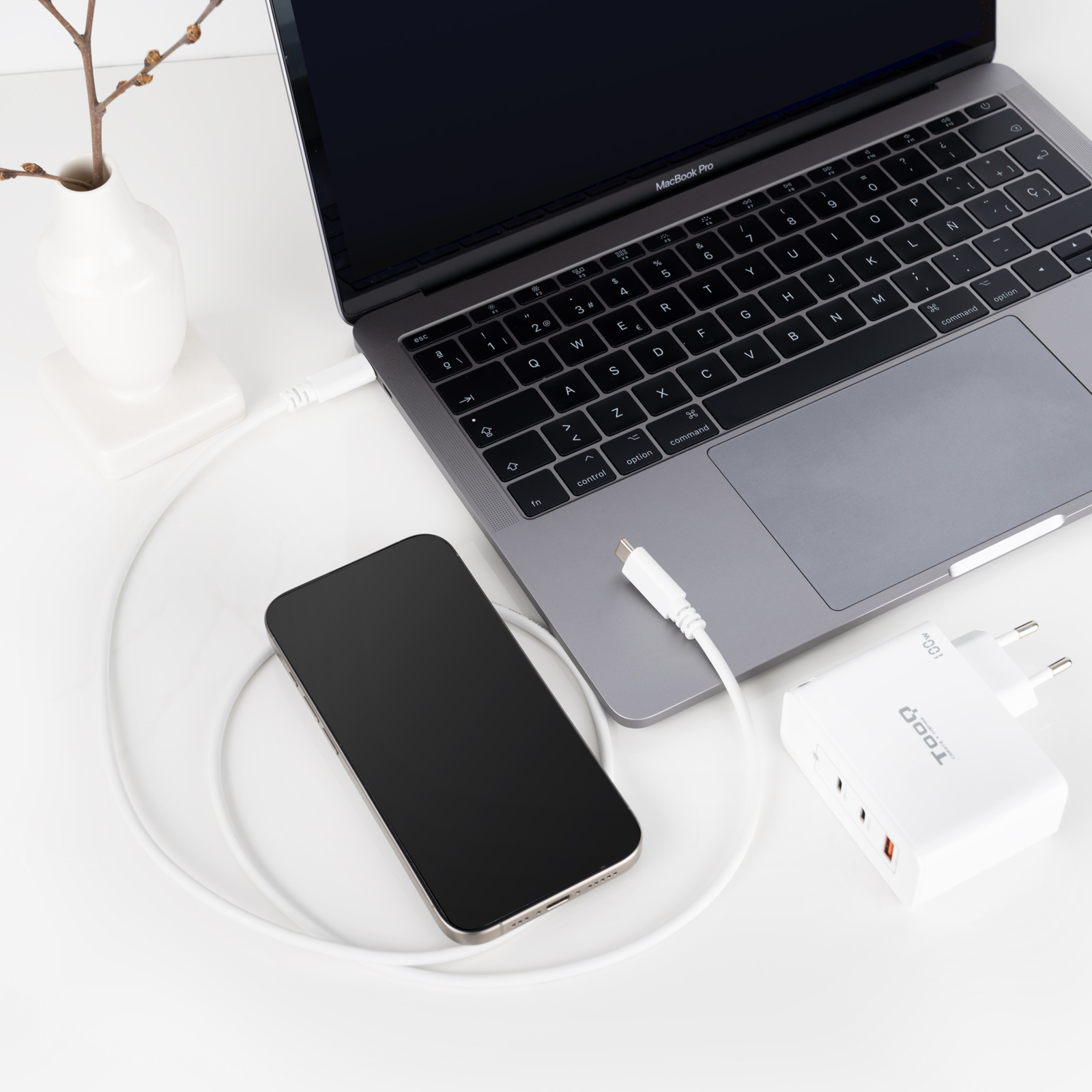 Laptop, telefoon en oplader. Laptop en oplader zijn verbonden via witte kabel. Telefoon ligt naast laptop.