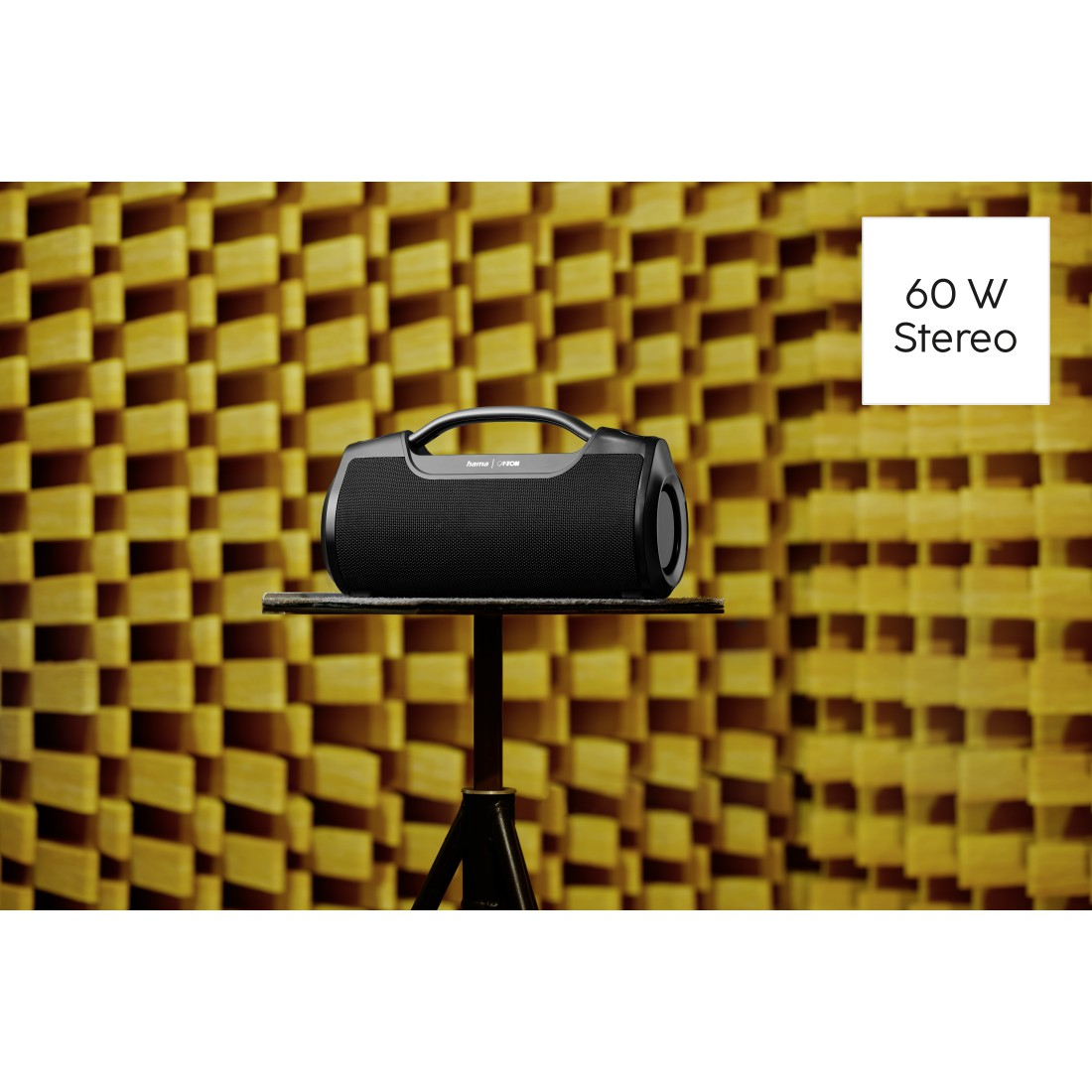 Un haut-parleur noir est posé sur un support devant un mur jaune insonorisé. Le texte indique '60 W Stereo'.