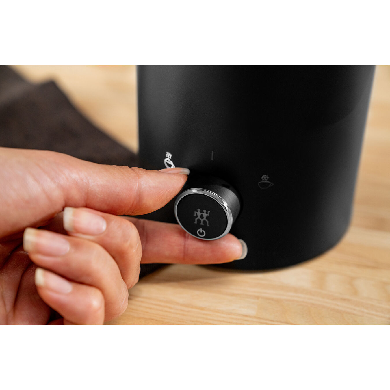 Dłoń obracająca pokrętło na czarnym urządzeniu. Pokrętło ma symbol.