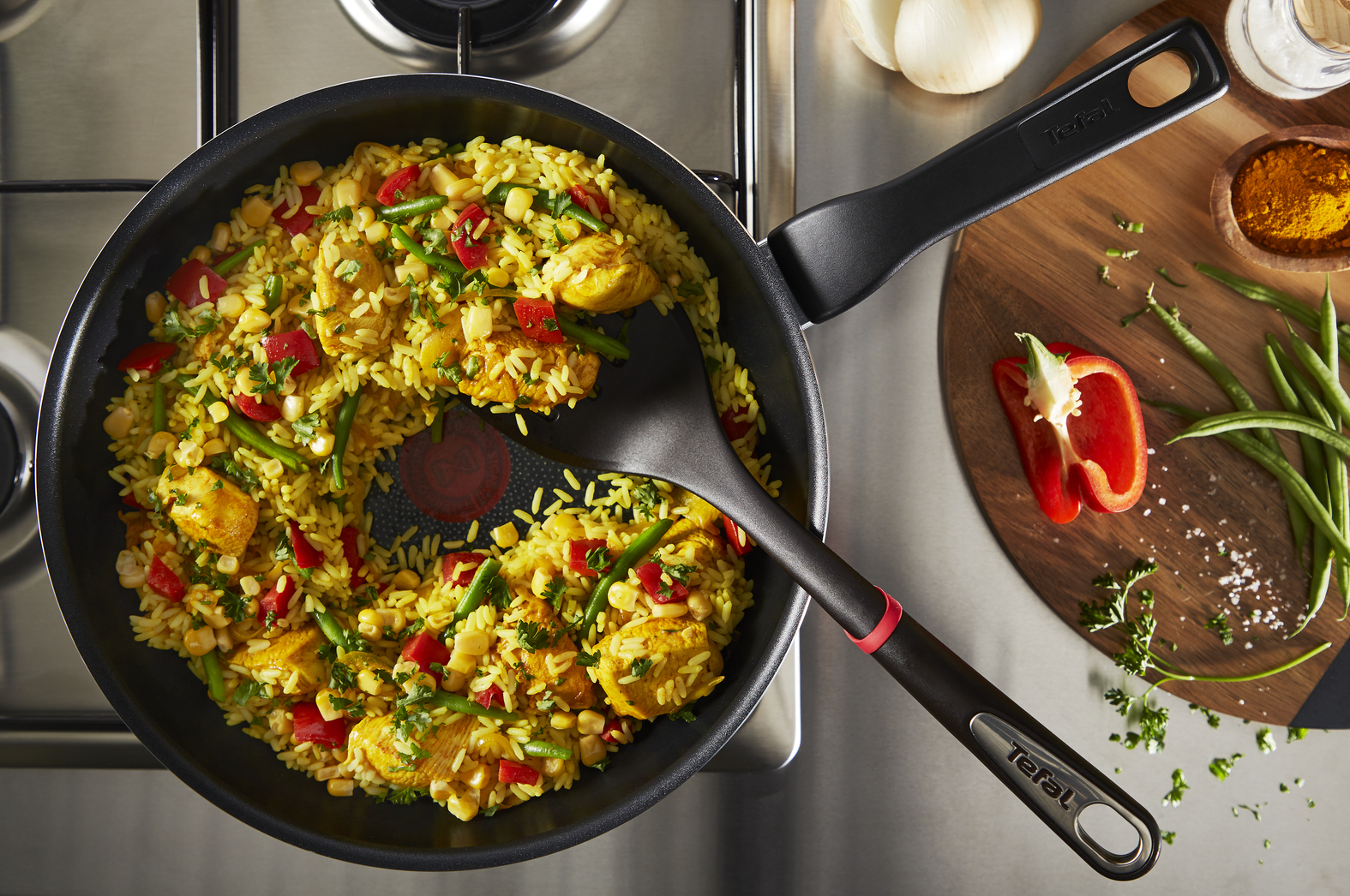 Widok z góry na patelnię z żółtym ryżem, warzywami i kurczakiem. Obok szpatułka i deska do krojenia.