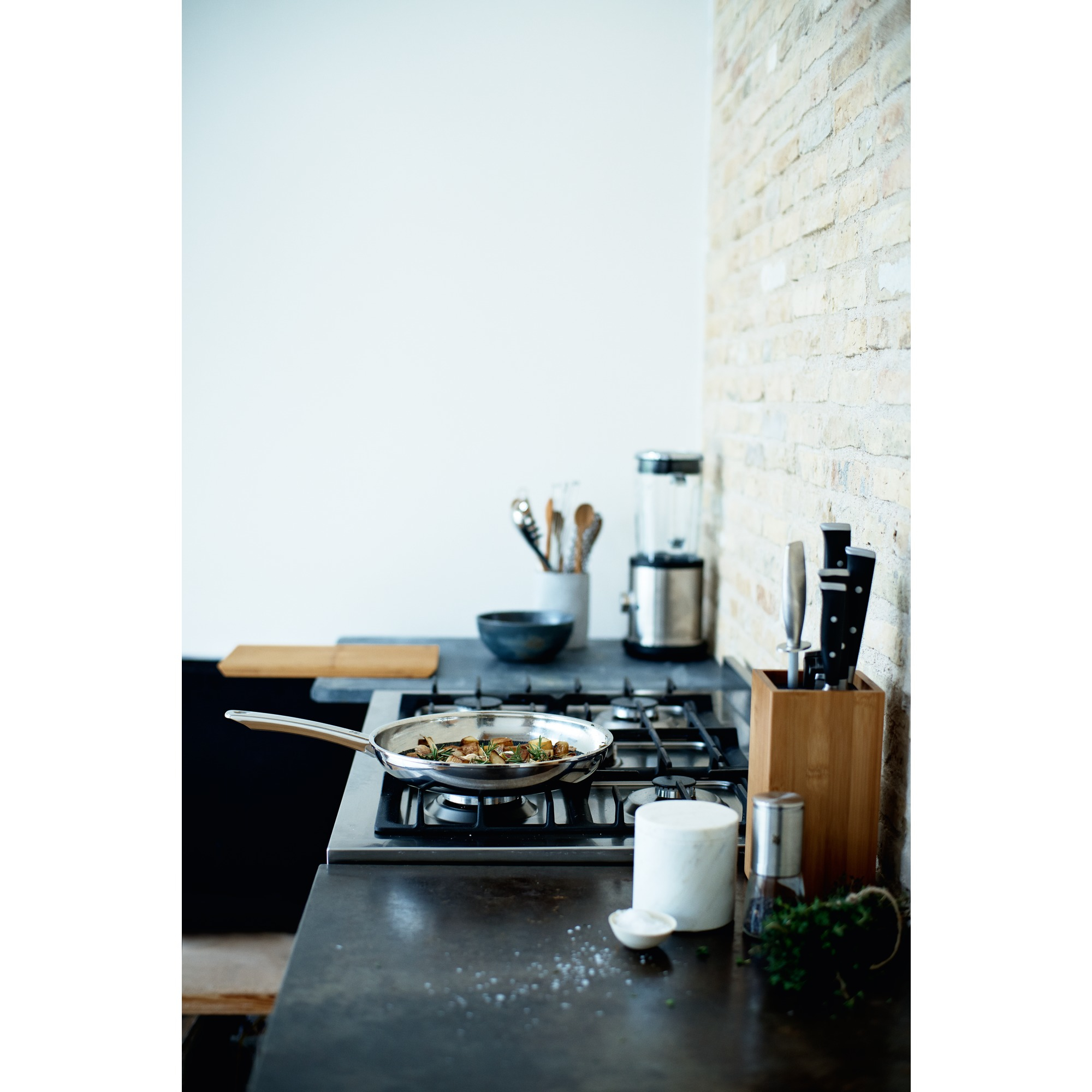 Patelnia z jedzeniem na kuchence, scena kuchenna z przyborami, blenderem i ceglaną ścianą.