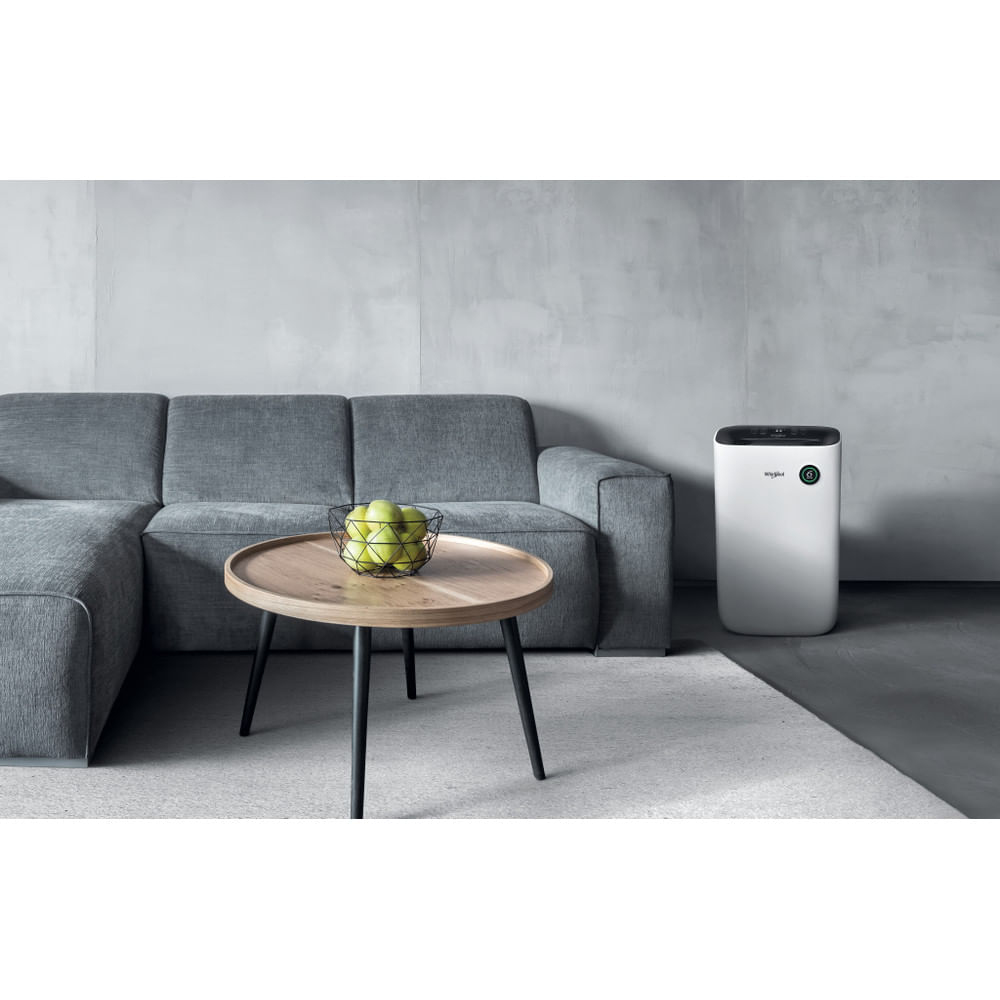 Wohnzimmerszene mit grauem Sofa, Holztisch und weißem Luftreiniger. Grüne Äpfel auf dem Tisch.