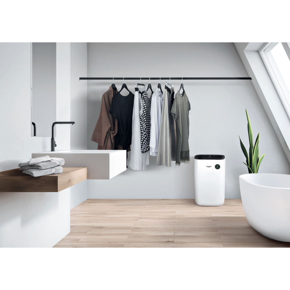 Ein Badezimmer mit Waschbecken, Spiegel und Kleidung auf einem Gestell. Es gibt auch einen weißen Luftentfeuchter.