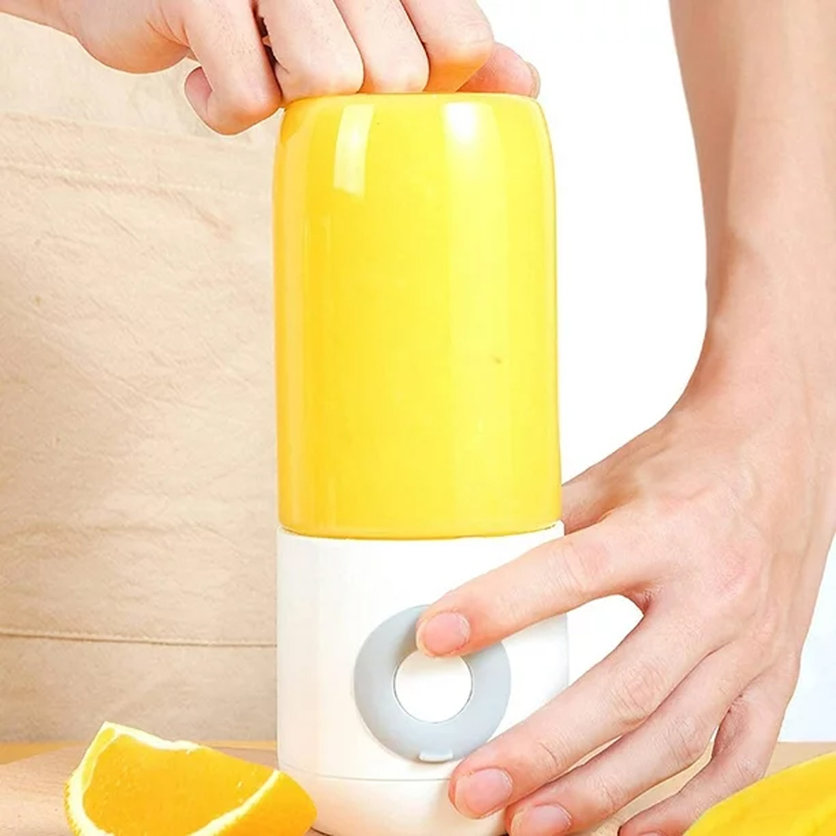 Hände, die einen gelben Mixer benutzen. Eine Orangenscheibe liegt in der Nähe auf einer weißen Oberfläche.