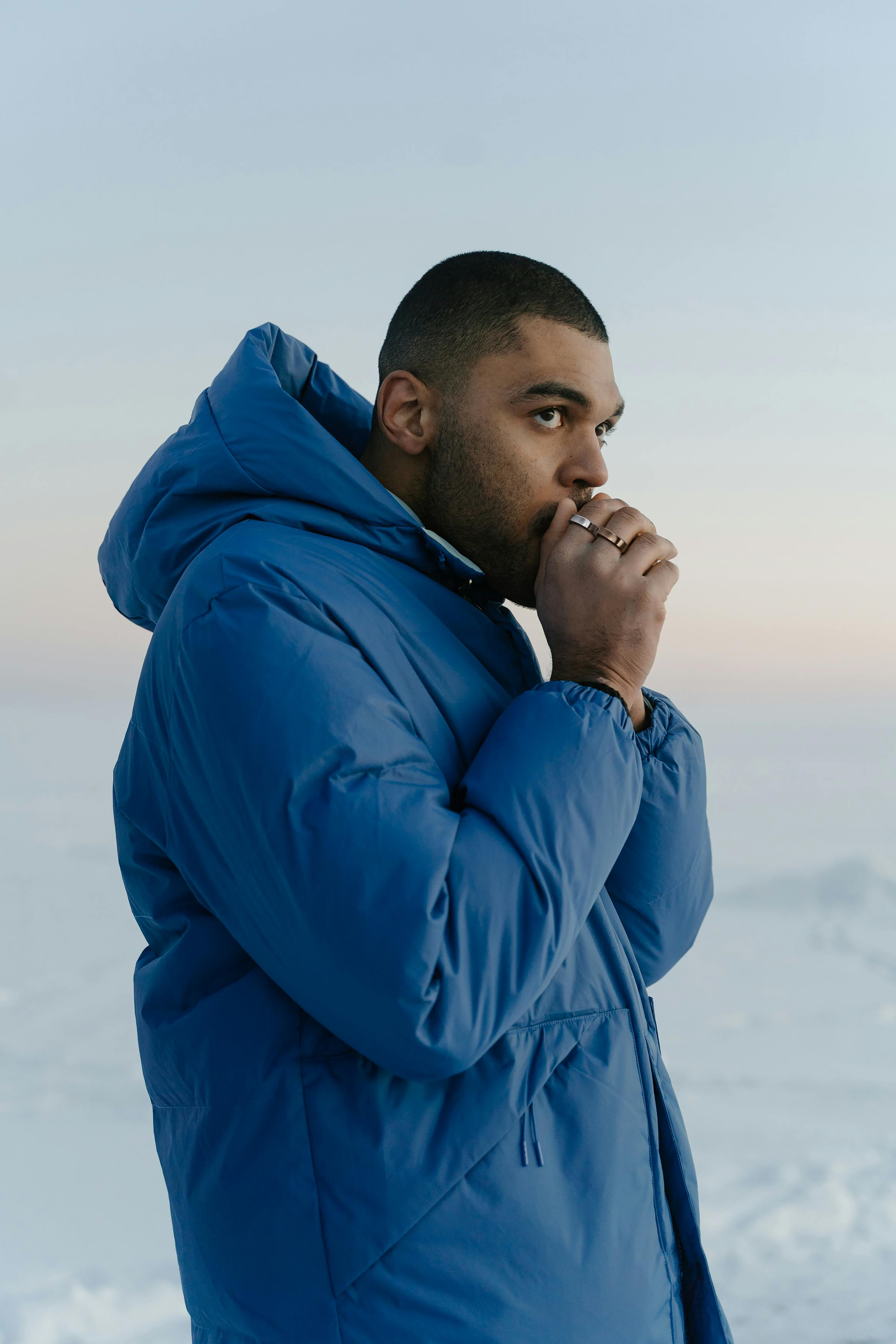 Ein Mann in einer blauen Jacke schaut weg und hält seine Hand vor sein Gesicht. Kalter, schneebedeckter Hintergrund.