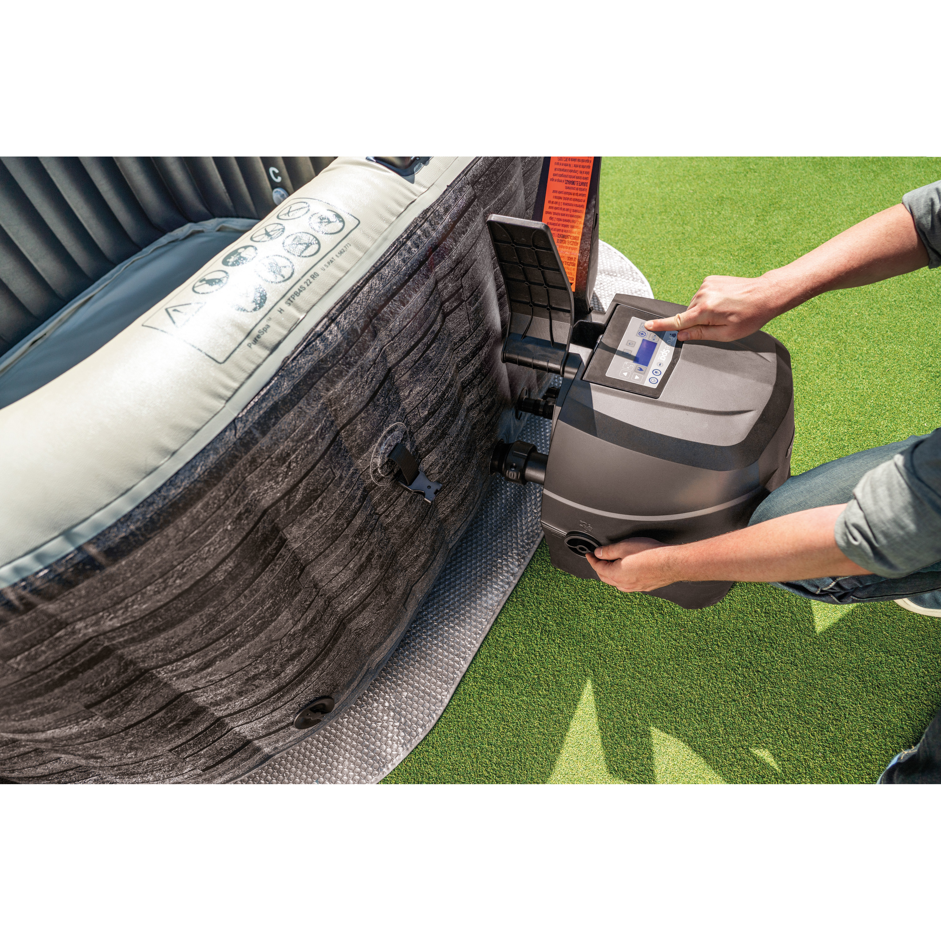 Osoba używająca pompy do jacuzzi przymocowanej do przenośnej wanny z hydromasażem na zielonej powierzchni.