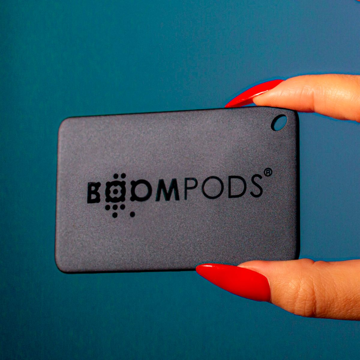 Una mano con unghie rosse tiene un rettangolo nero con la scritta 'BOOMPODS'.