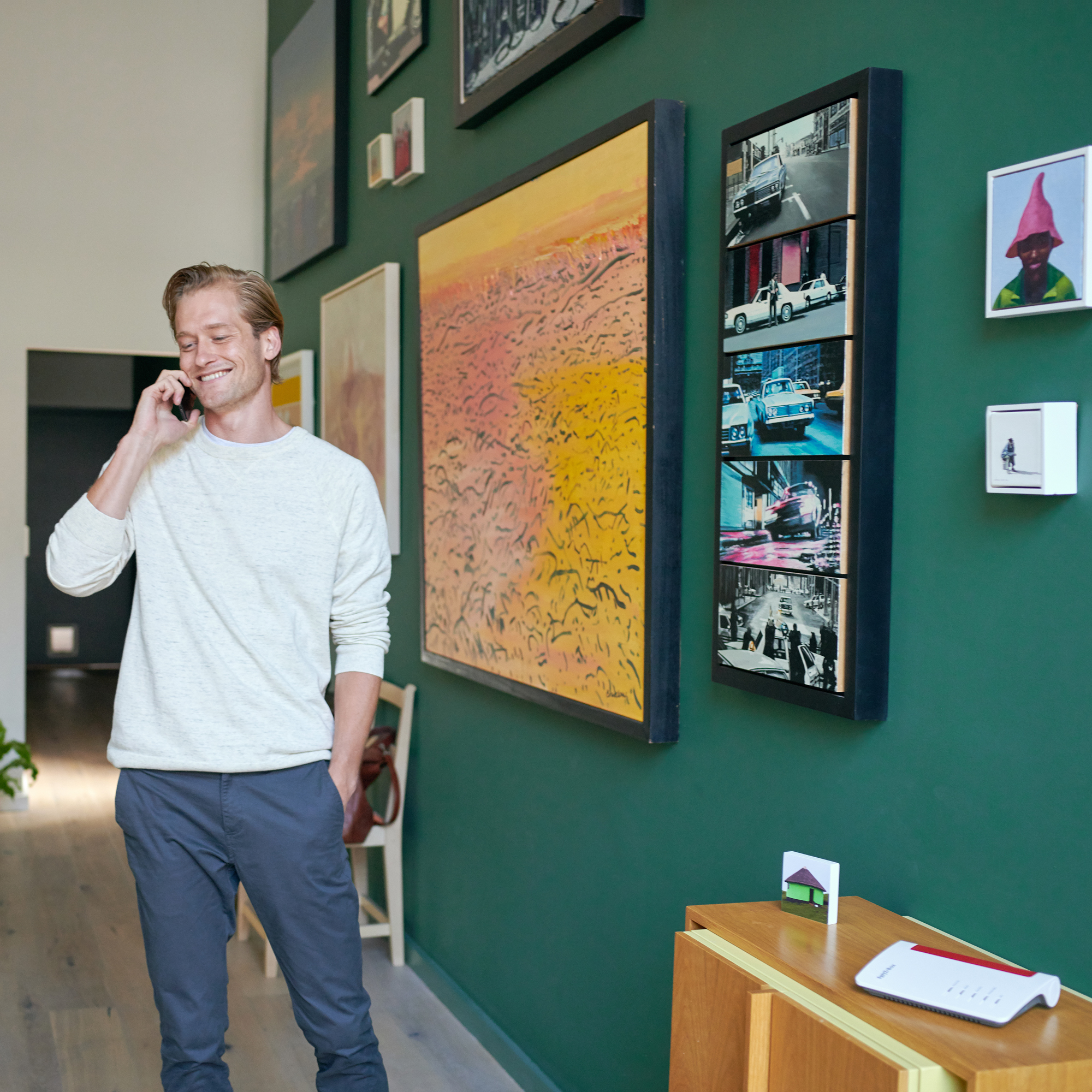 Mężczyzna w pokoju rozmawia przez telefon. Sztuka na ścianach. Router na stole.