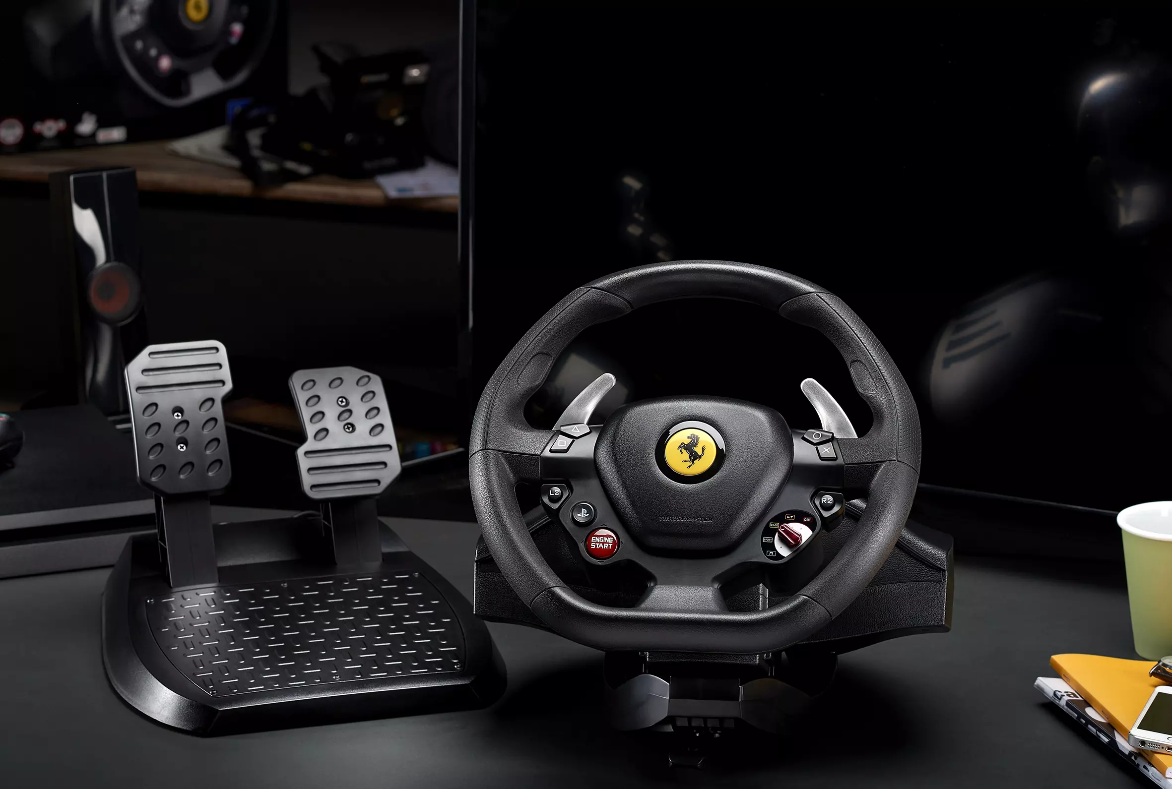 Ferrari-Rennlenkrad mit Pedalen, auf einem schwarzen Schreibtisch.