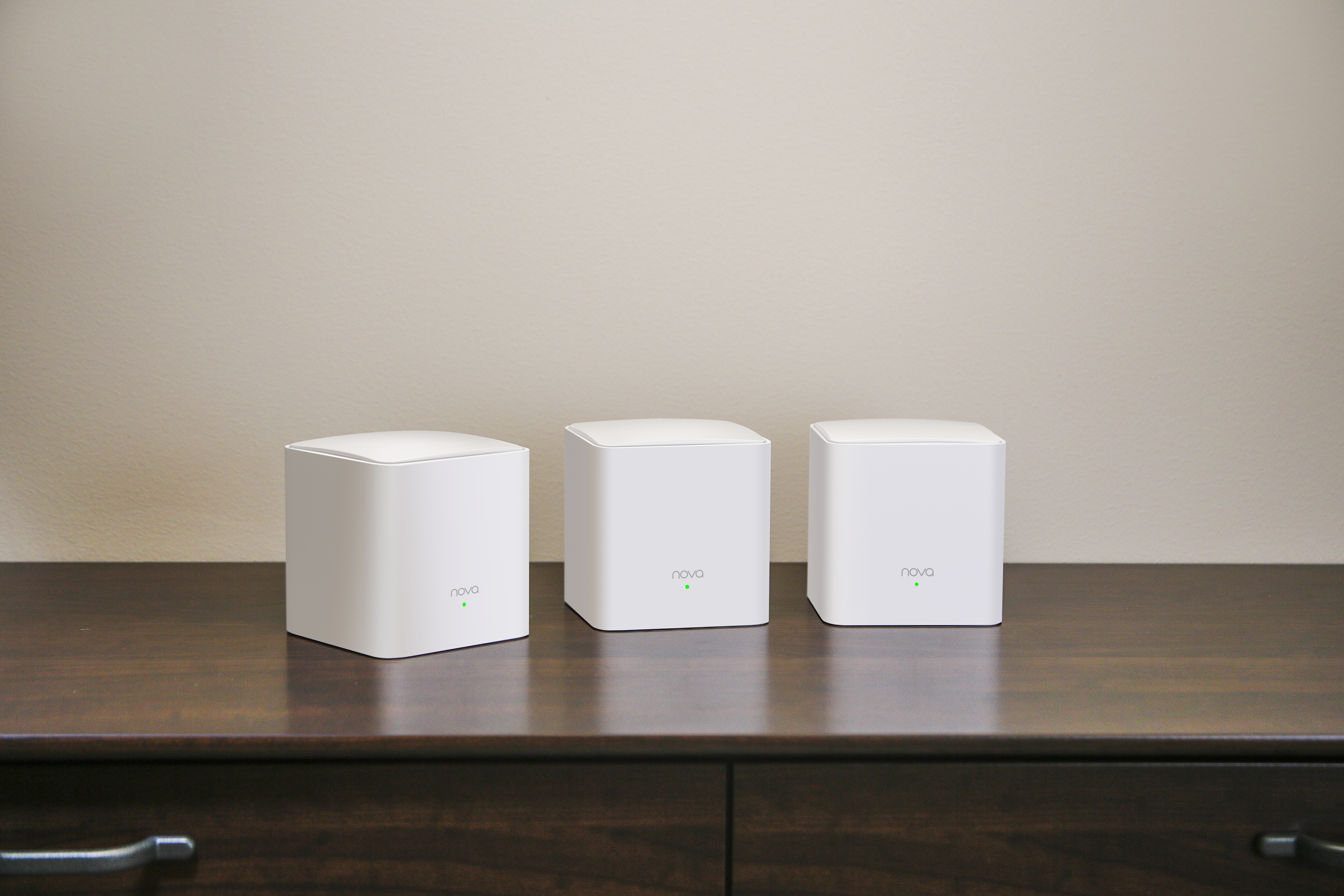 Tre router WiFi a mesh bianchi su un tavolo in legno scuro, parete beige sullo sfondo.