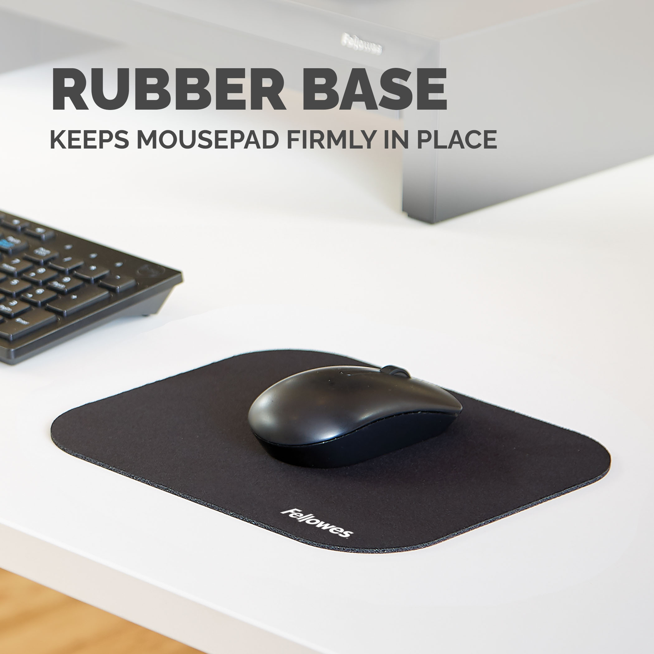 Une souris noire sur un tapis de souris noir. Un clavier est en arrière-plan.