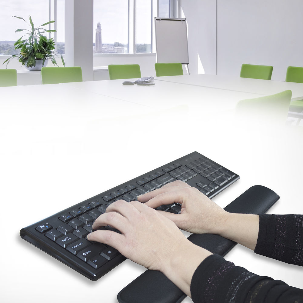 Hands typing on a keyboard with a wrist rest in an office setting.  A meeting is in the background.