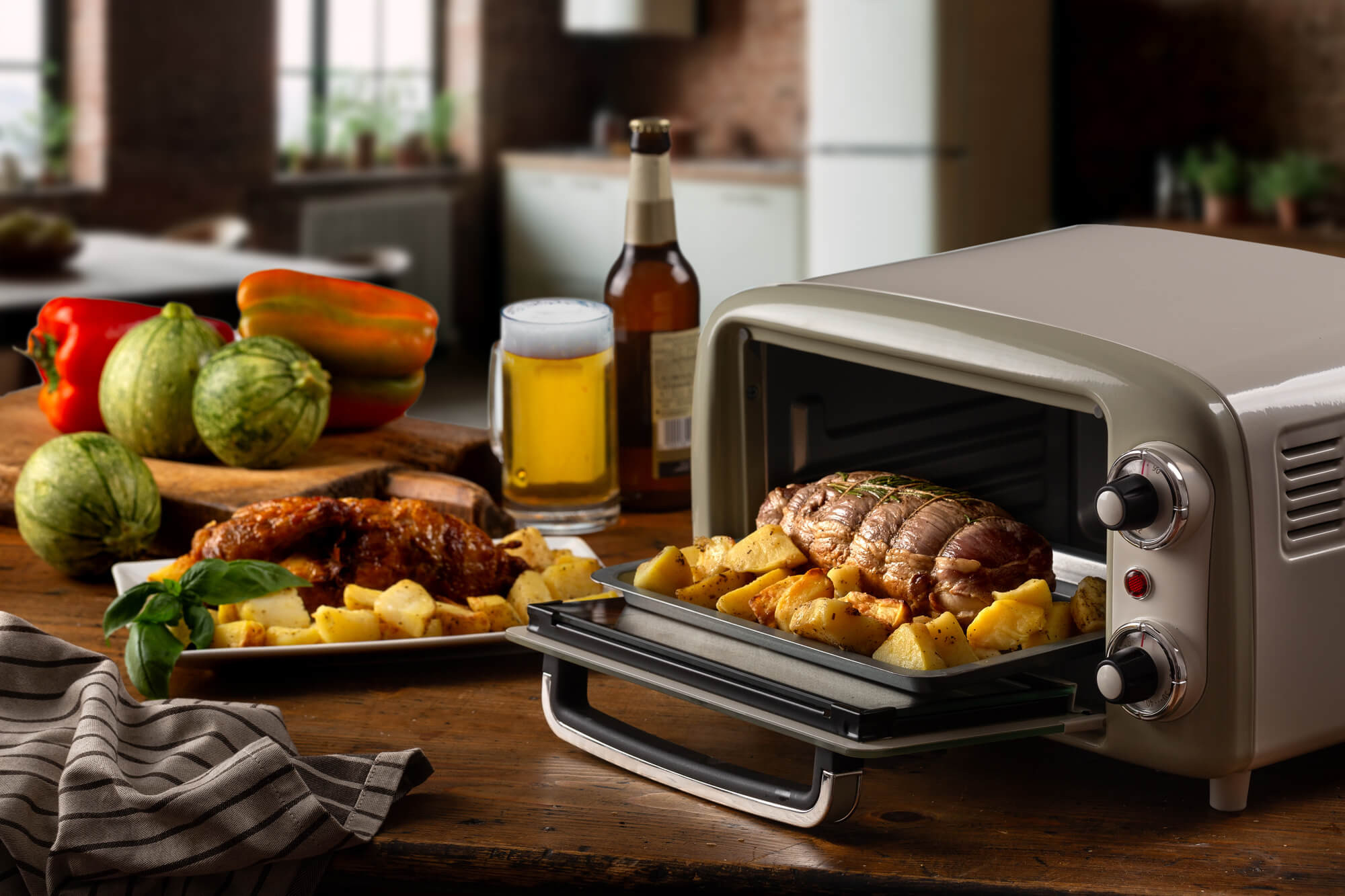 Szary piekarnik z jedzeniem na tacy. Warzywa, piwo i talerz z jedzeniem na stole.