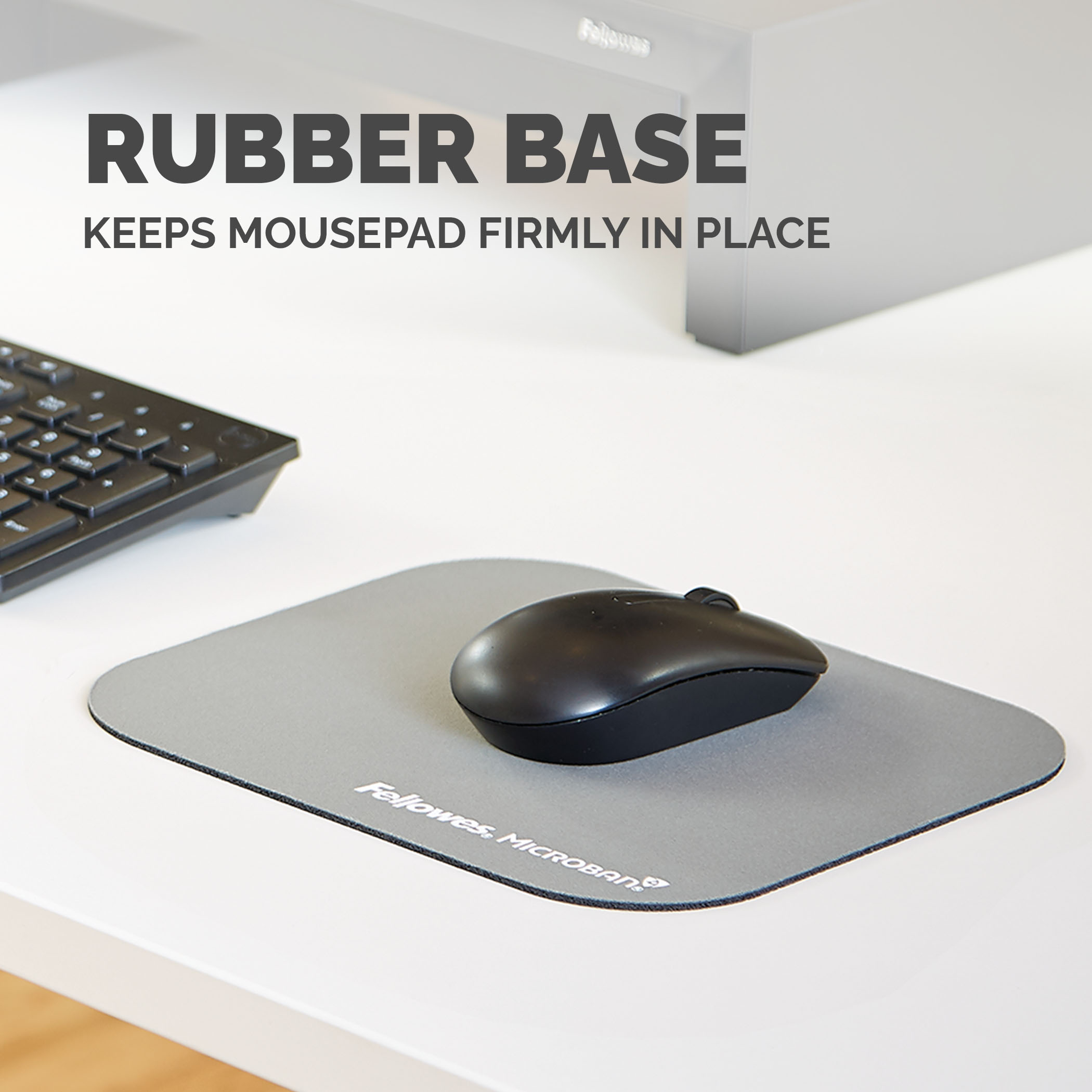 Un tappetino per il mouse grigio con un mouse nero e una tastiera sullo sfondo.