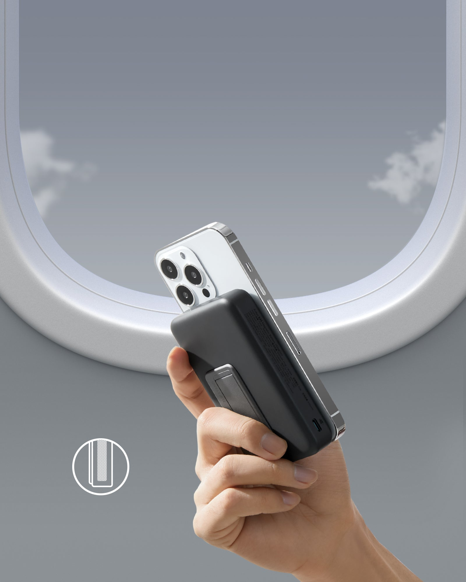 Eine Hand, die ein Telefon mit einer schwarzen Powerbank hält; Hintergrund eines Flugzeugfensters.