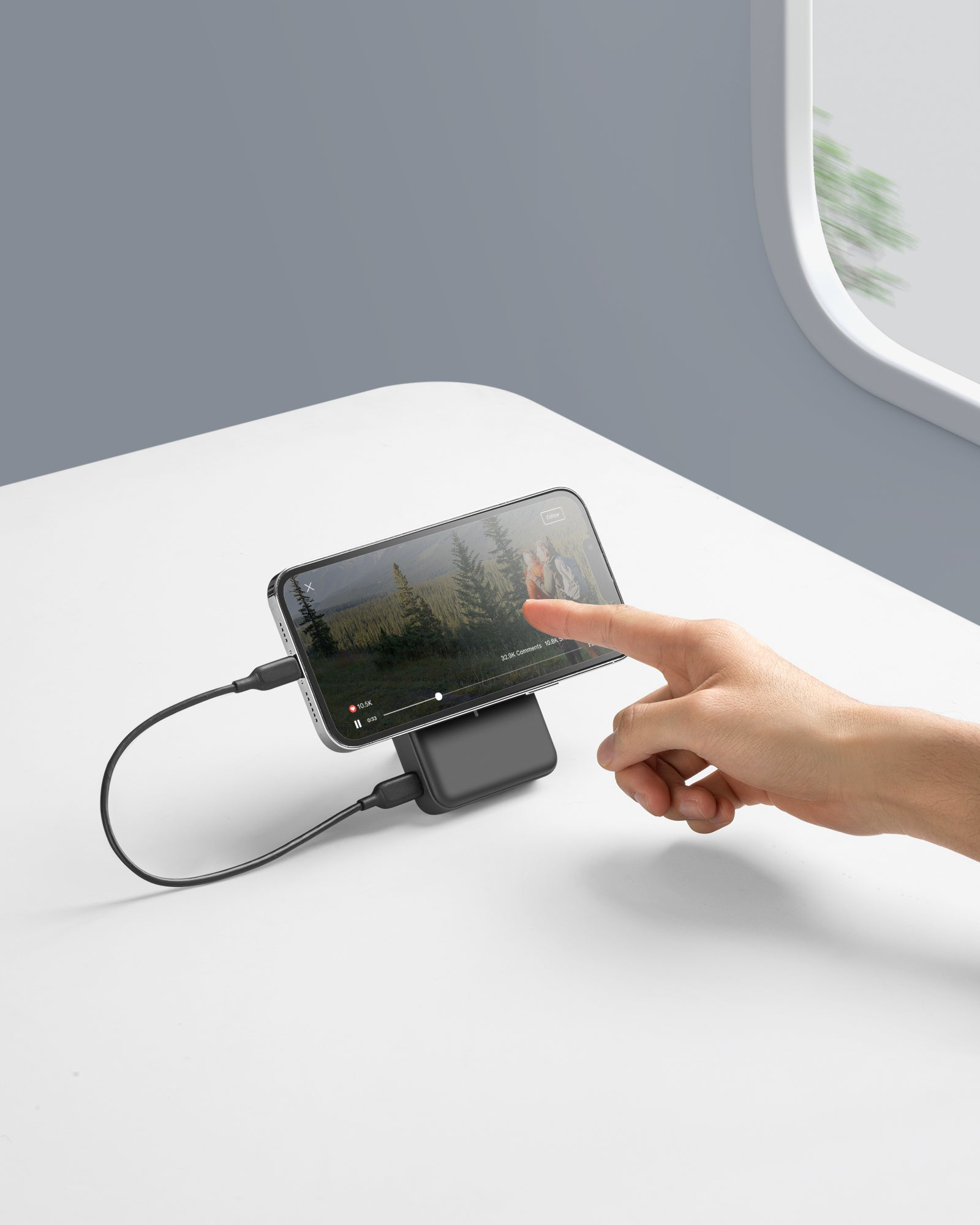 Ein Telefon auf einem Ständer spielt ein Video ab. Eine Hand berührt den Bildschirm. Ein Ladekabel ist angeschlossen.