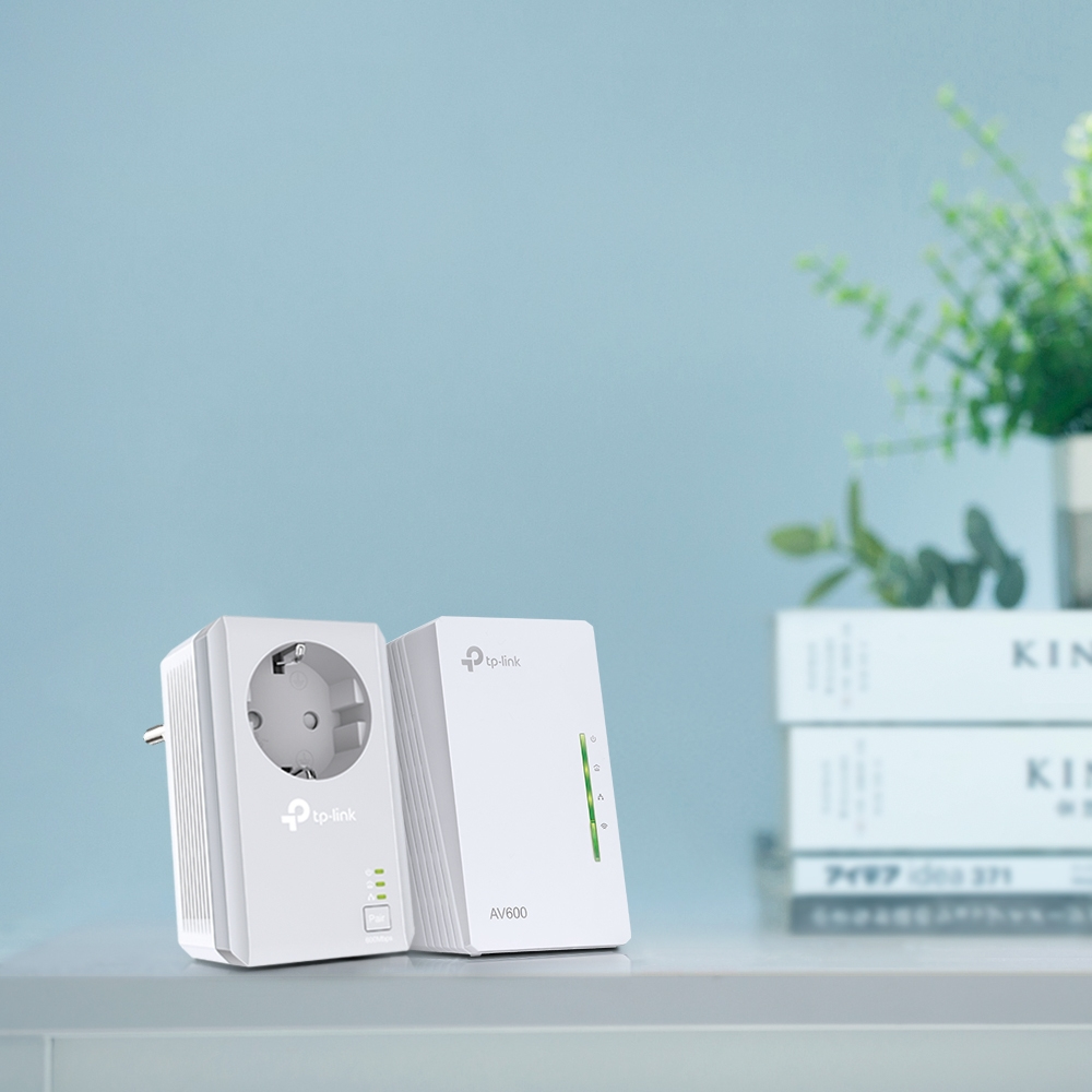 Dwa białe adaptery sieciowe TP-Link z rośliną w tle.