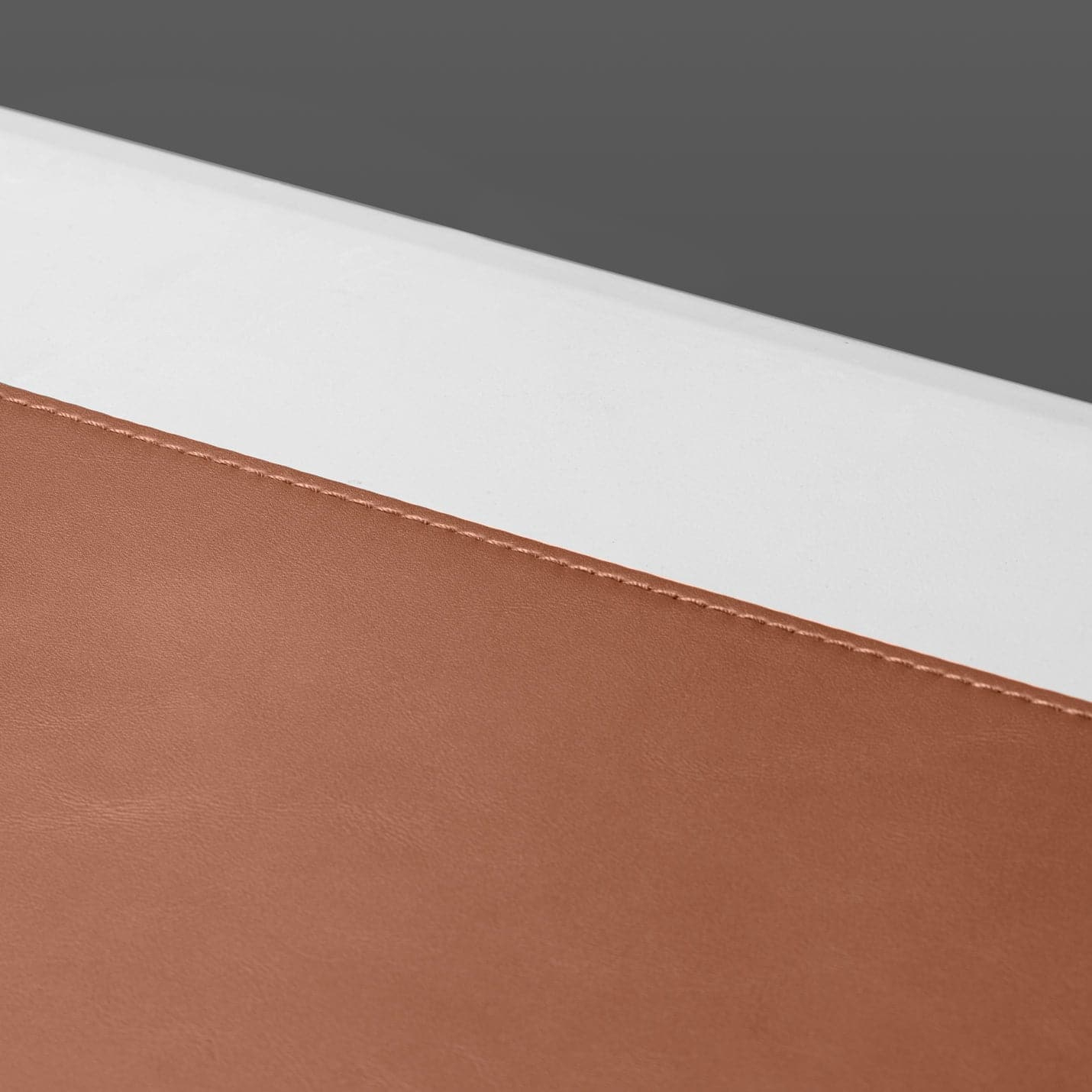 Tapis de souris en cuir marron avec bord blanc. Le tapis de souris est sur une surface blanche.
