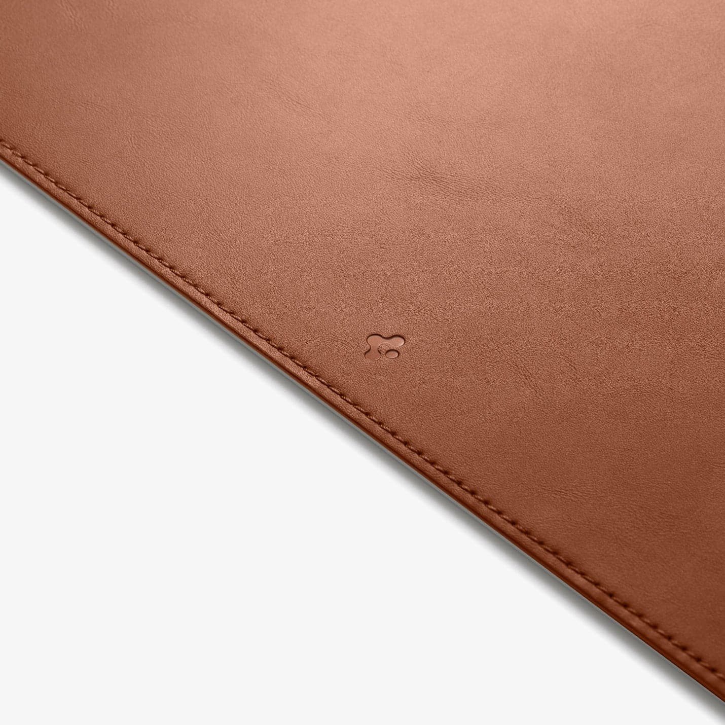 Tapis de souris en cuir marron, gros plan sur le logo. Le tapis de souris est sur une surface blanche.