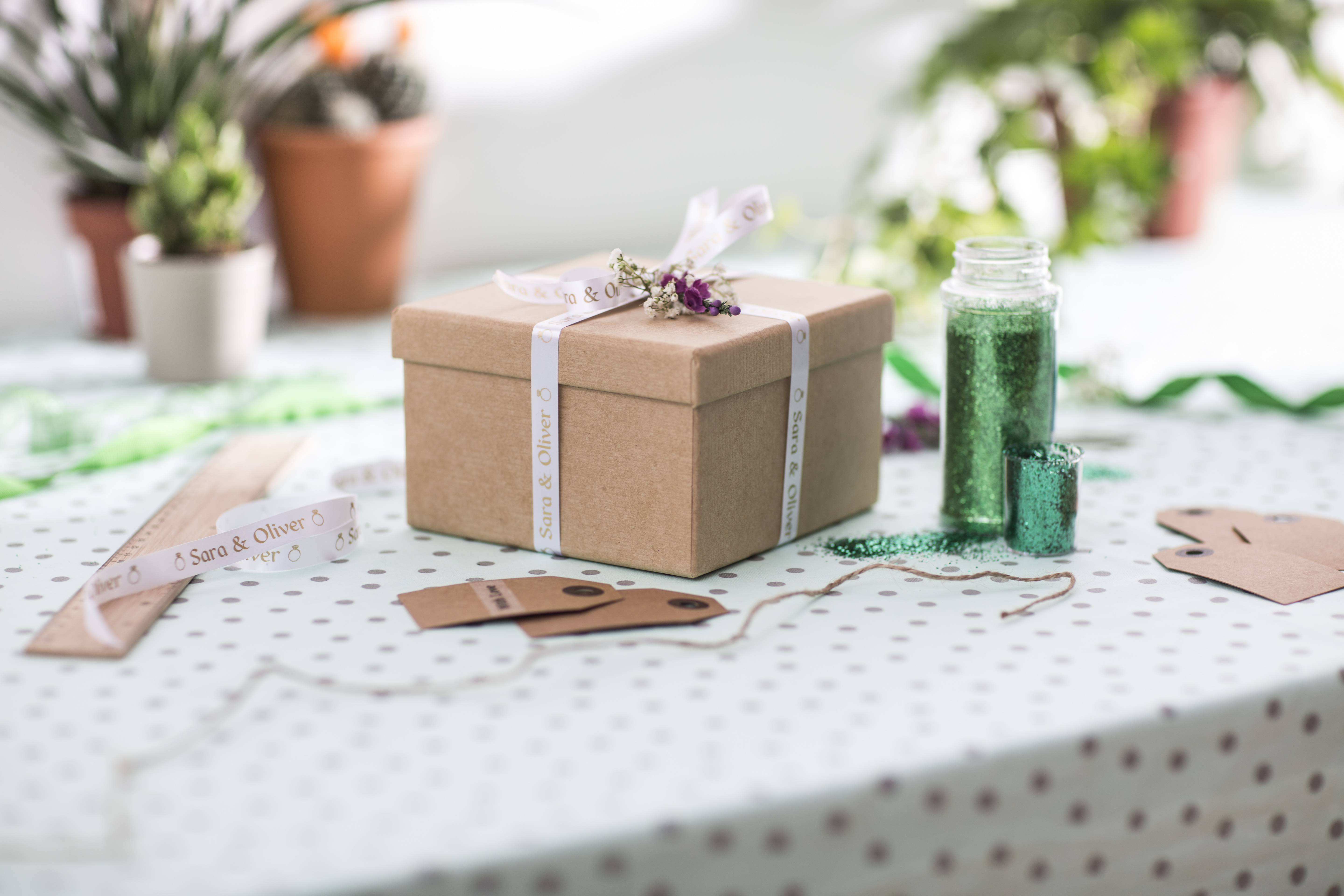 Eine Geschenkbox auf einem Tisch. Auf der Box befinden sich Schleifen und Blumen. Andere Artikel sind in der Nähe.