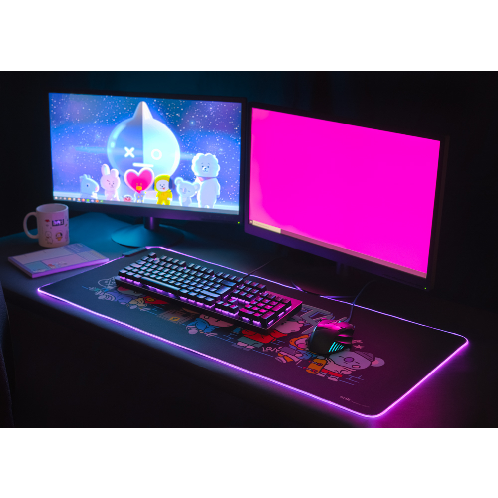 Ein Gaming-Setup mit zwei Monitoren, einer Tastatur und einer Maus auf einem großen Mauspad mit Cartoon-Design.