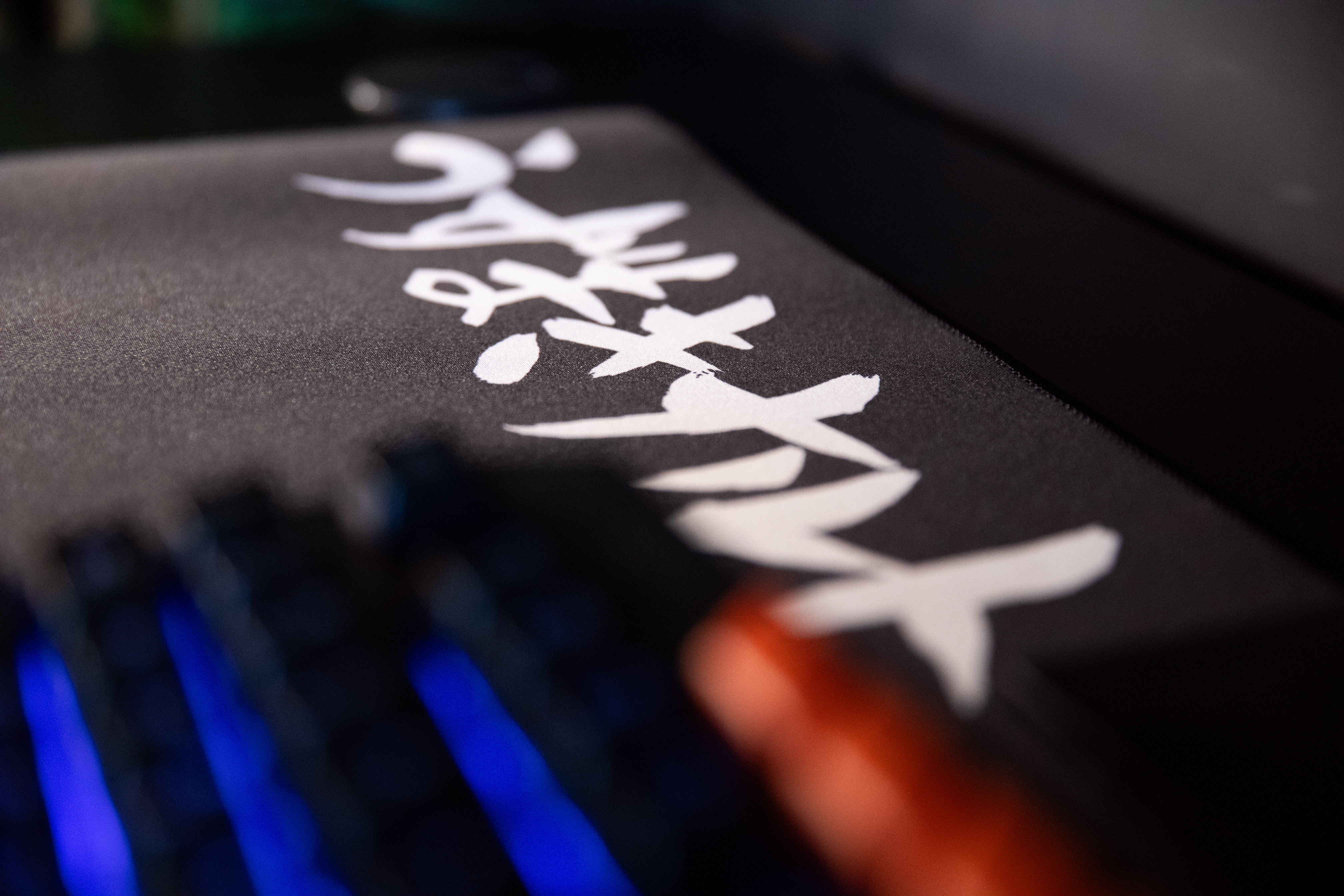 Czarna podkładka pod mysz z białymi japońskimi znakami. Niebieska klawiatura widoczna.