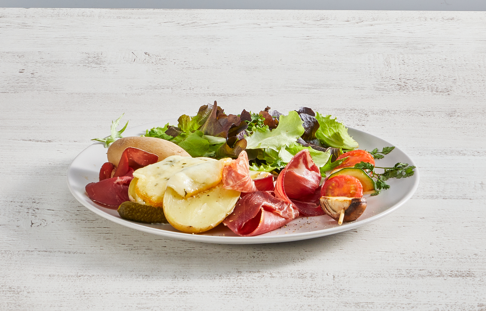 Talerz z różnymi produktami spożywczymi: sałatą, ziemniakami, mięsem i serem. Białe drewniane tło.