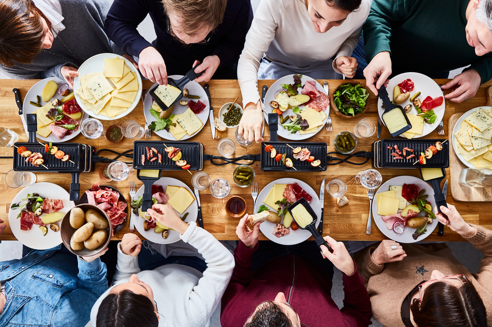 Widok z góry na grupę ludzi jedzących Raclette. Jedzenie i grille do raclette na stole.
