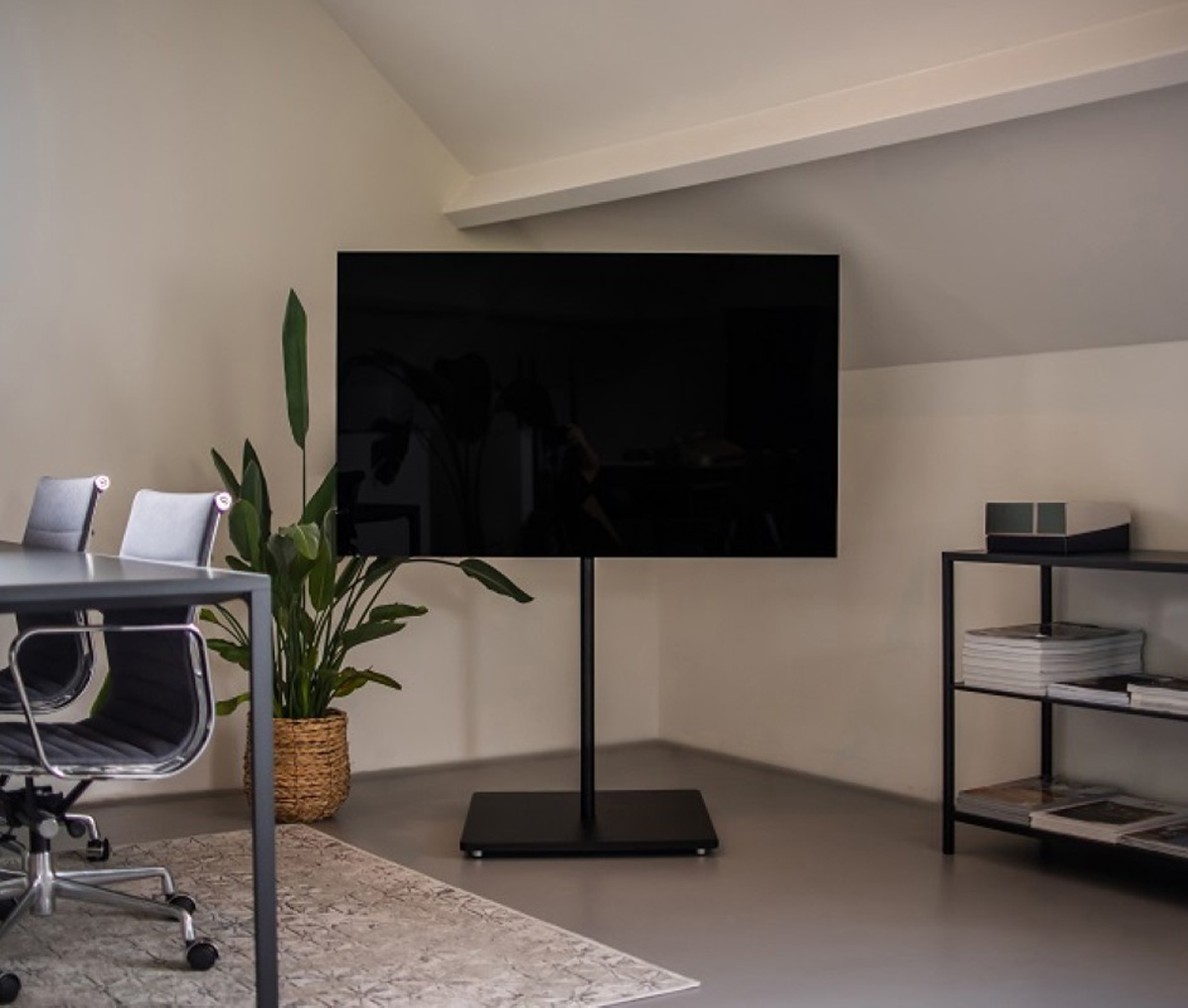 Grote zwarte tv op een standaard in een kamer met een bureau en een plant. Neutrale kleuren.