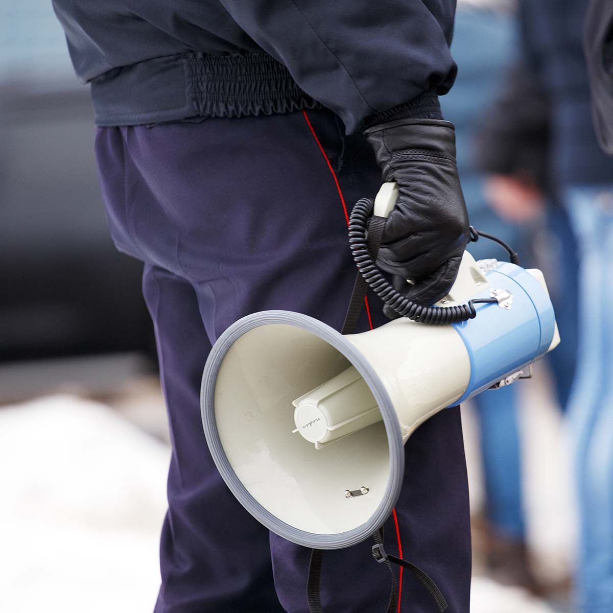 Une personne en uniforme de police tenant un mégaphone blanc et bleu avec un câble en spirale.