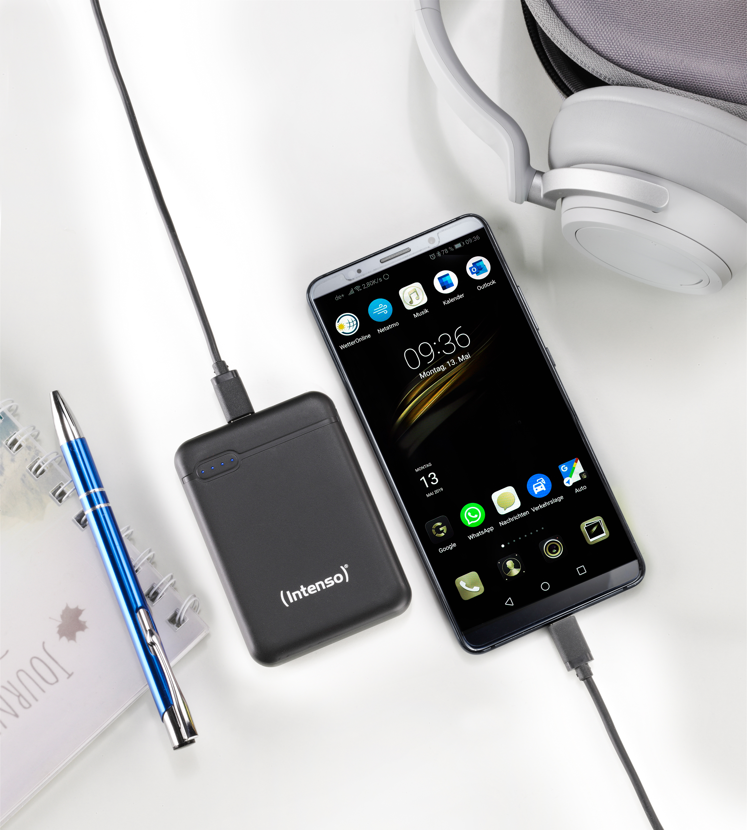 Smartphone die oplaadt vanaf een zwarte powerbank. Blauwe pen en notitieblok op wit oppervlak.