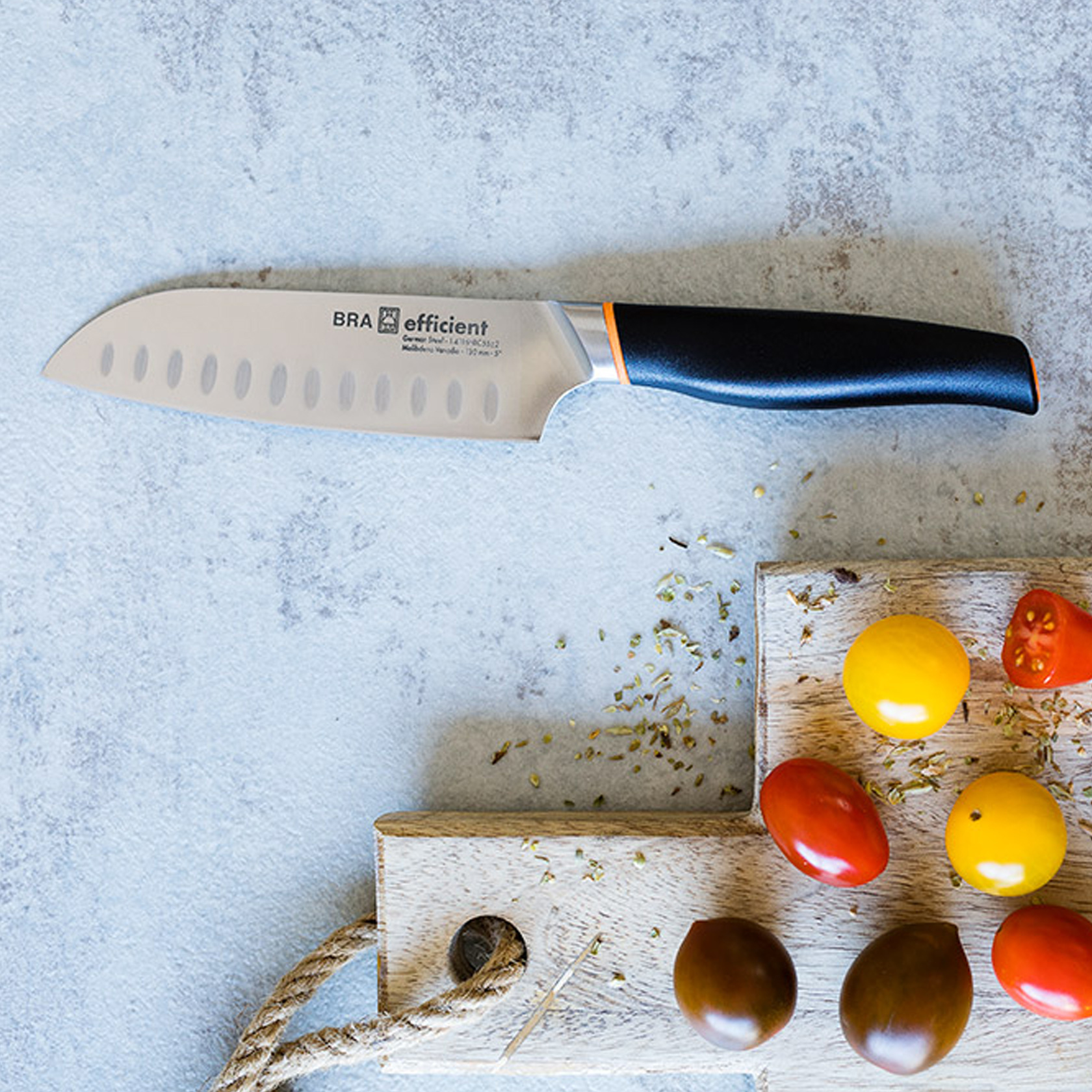 Nóż kuchenny na drewnianej desce do krojenia z pomidorami i ziołami. Czarny i pomarańczowy uchwyt.