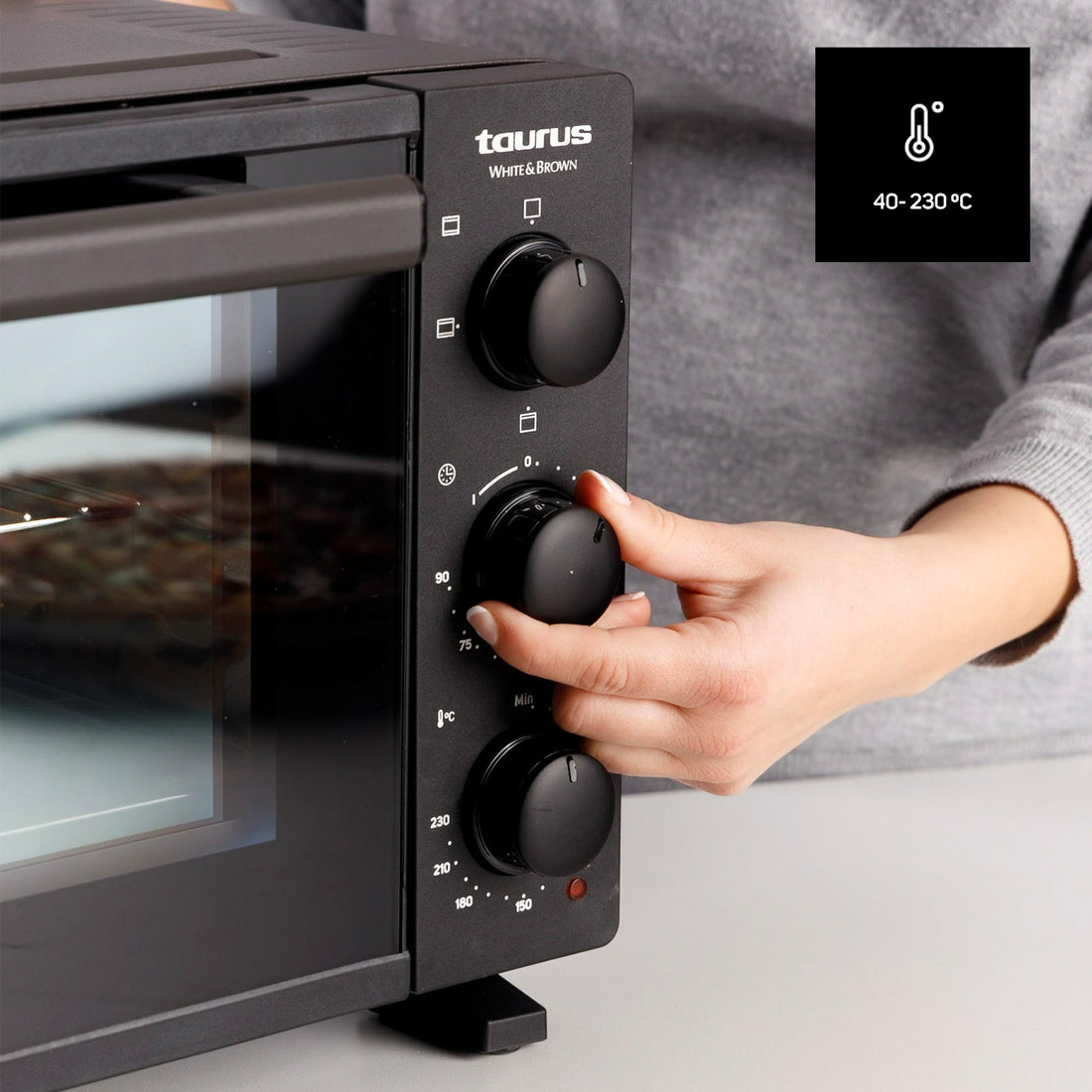Persona ajustando la temperatura del horno, horno negro con logo Taurus White & Brown.