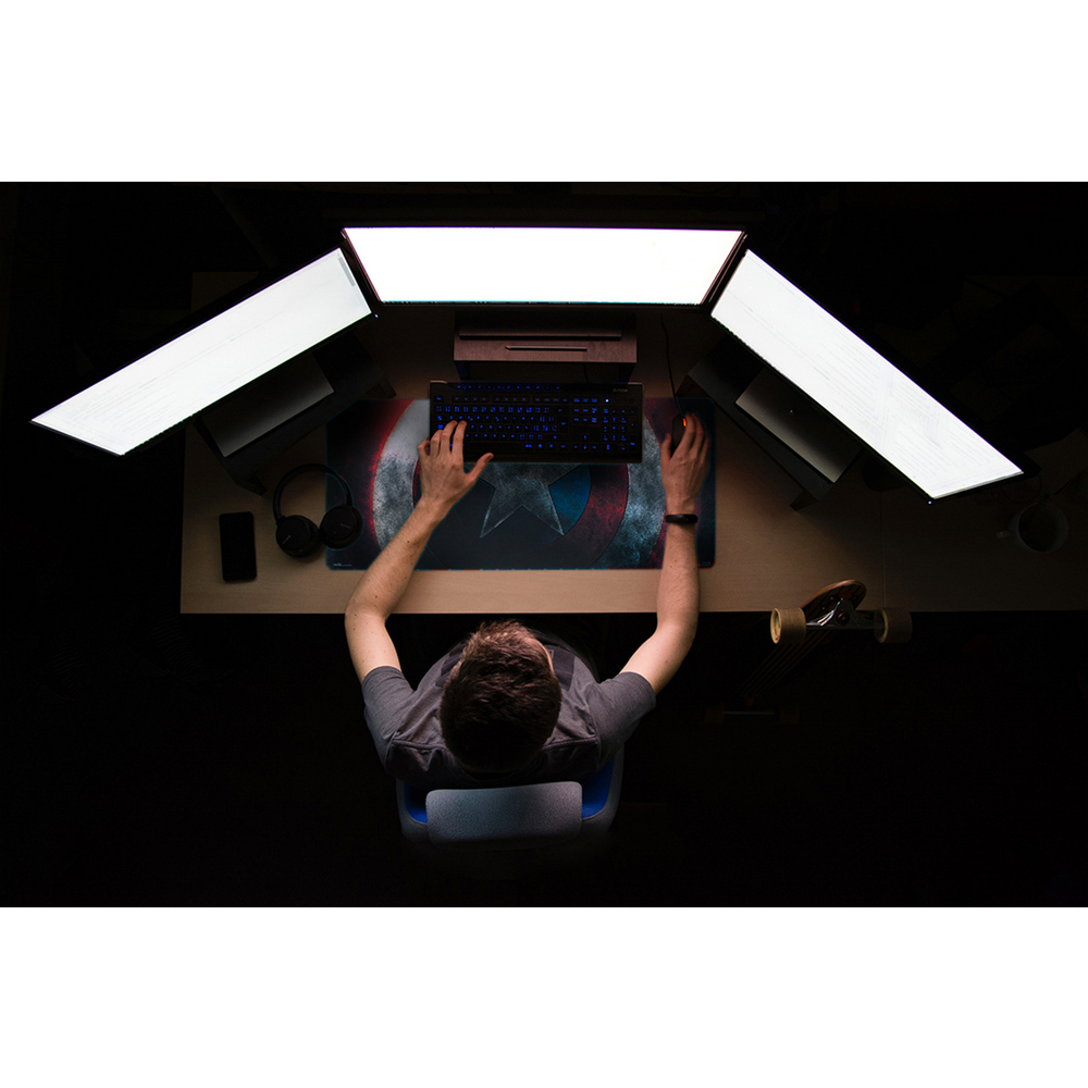 Eine Person arbeitet an einem Schreibtisch mit mehreren Monitoren und einer Tastatur.