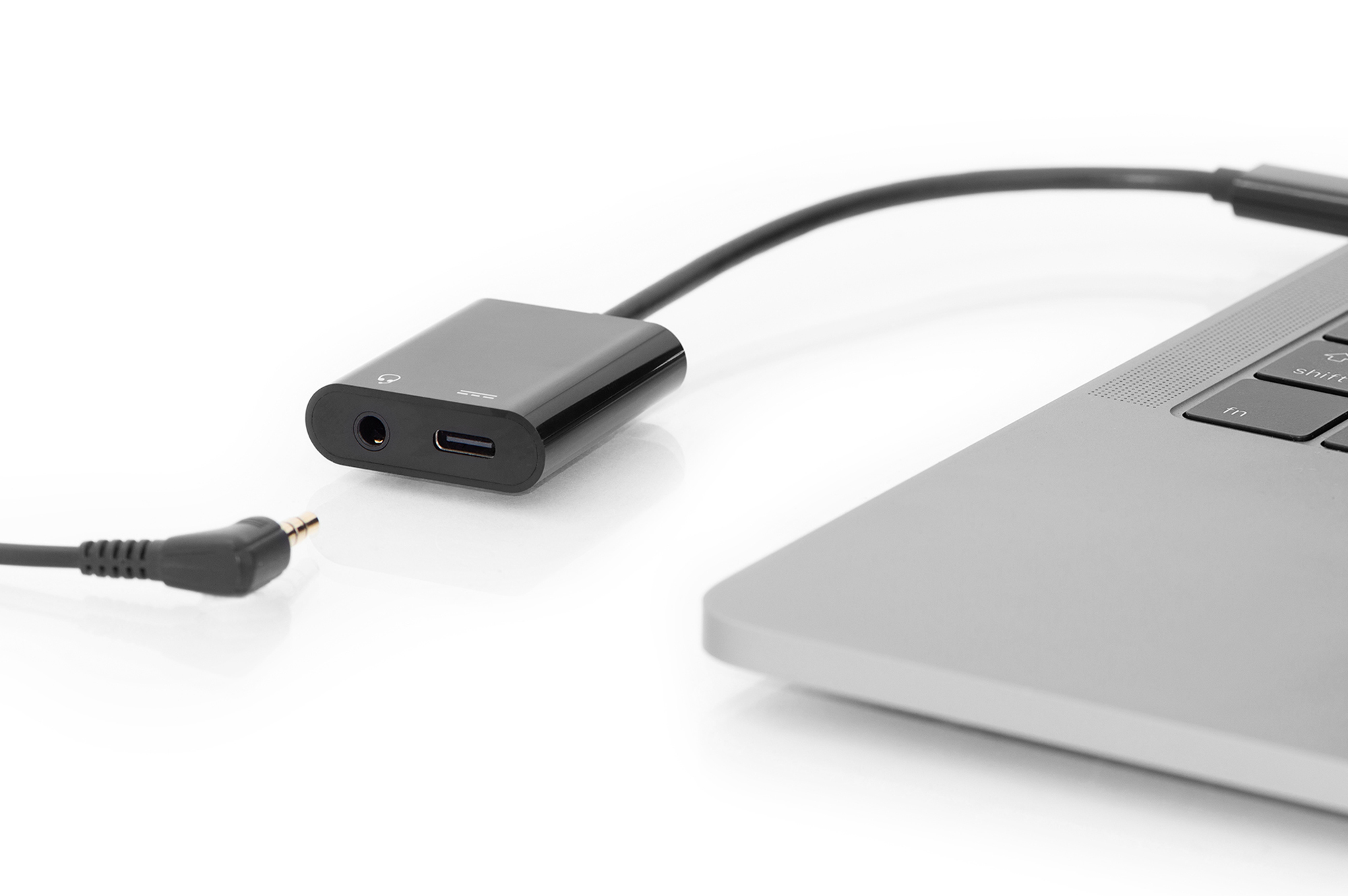 Ein schwarzer Adapter verbindet sich mit einem Laptop und einer 3,5-mm-Buchse. Der Laptop ist silber.