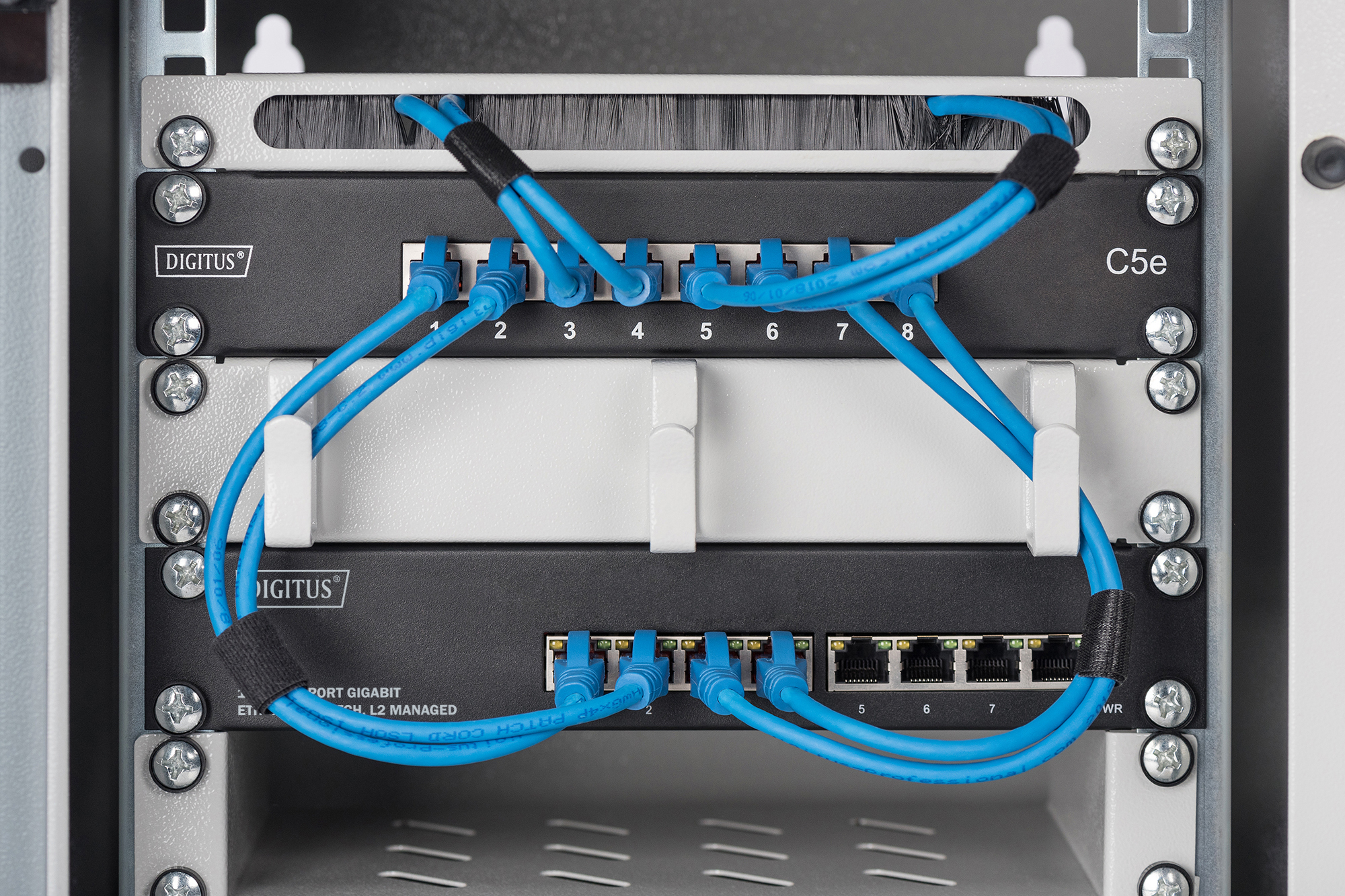 Netzwerkschrank mit blauen Netzwerkkabeln und angeschlossenen Geräten.