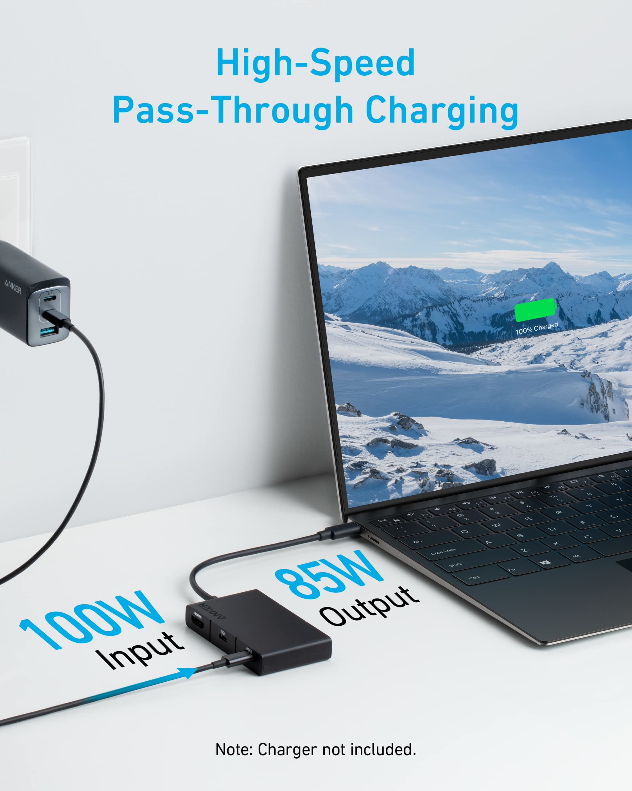 Laptop in carica con caricatore e hub. Il testo dice ingresso 100W e uscita 85W. Montagna innevata.