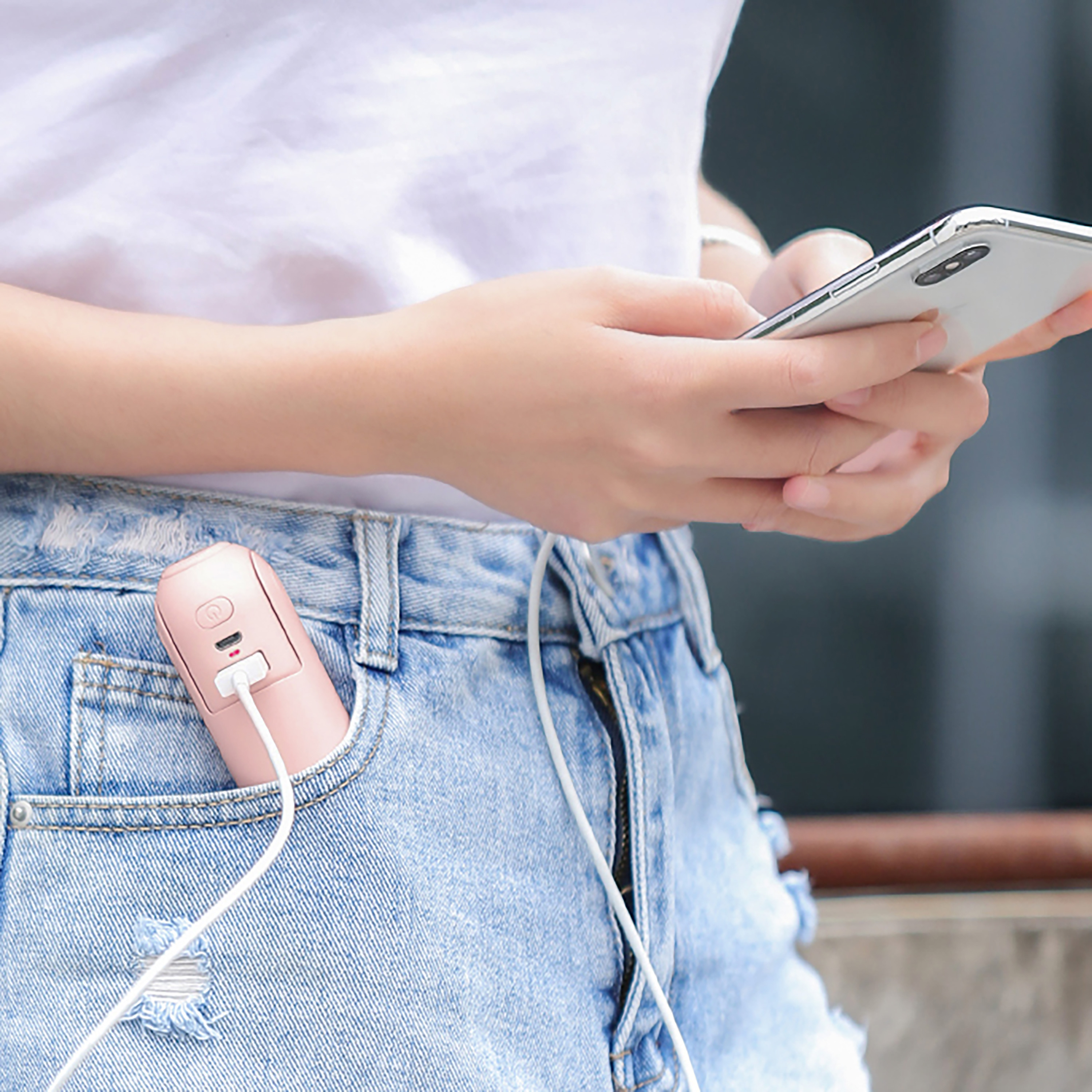 Beyaz gömlekli bir kişi telefon tutuyor, cebinde pembe bir taşınabilir şarj cihazı var.
